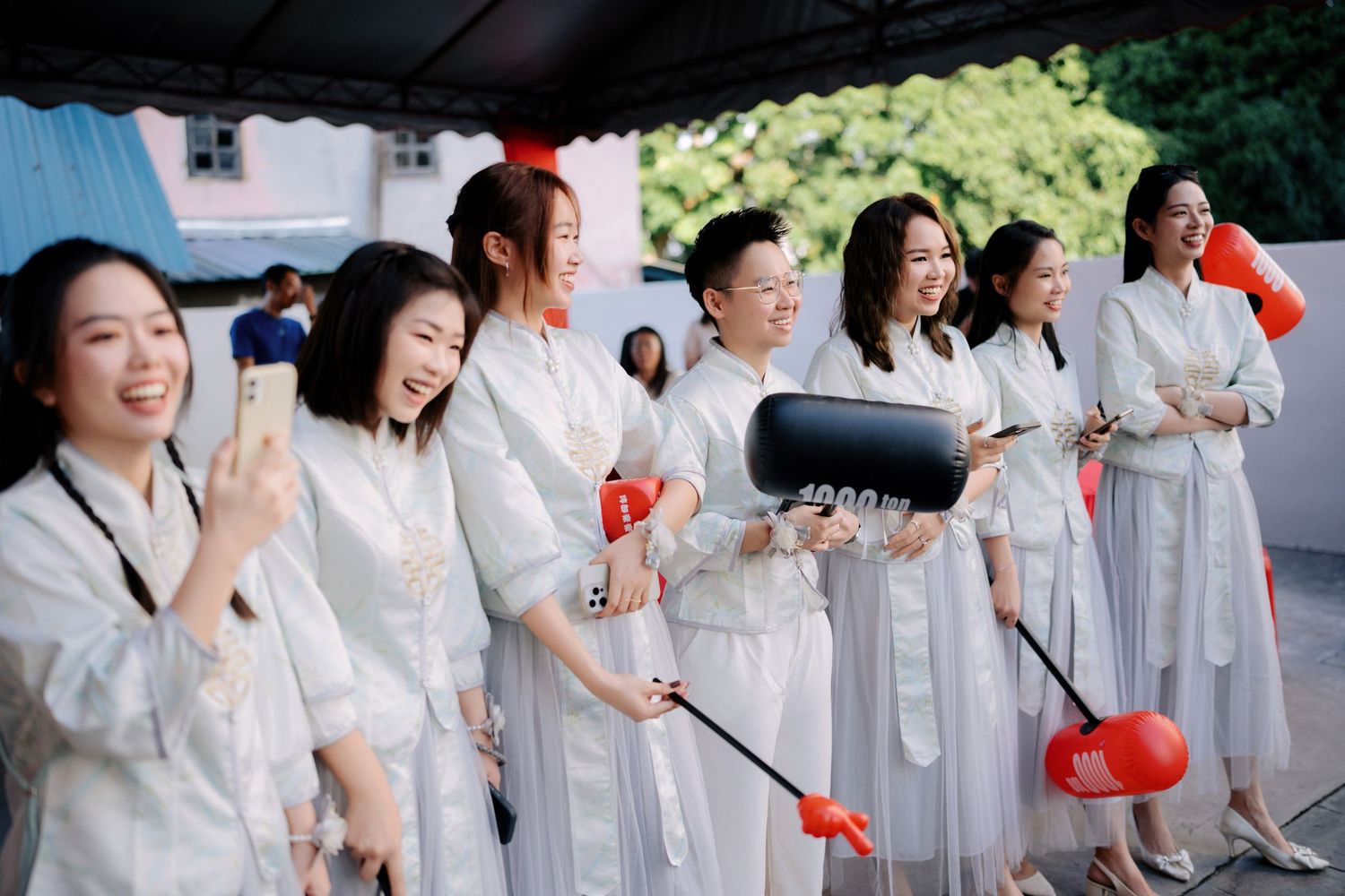 A group in white outfits poses outdoors holding red decorative items during a celebration.