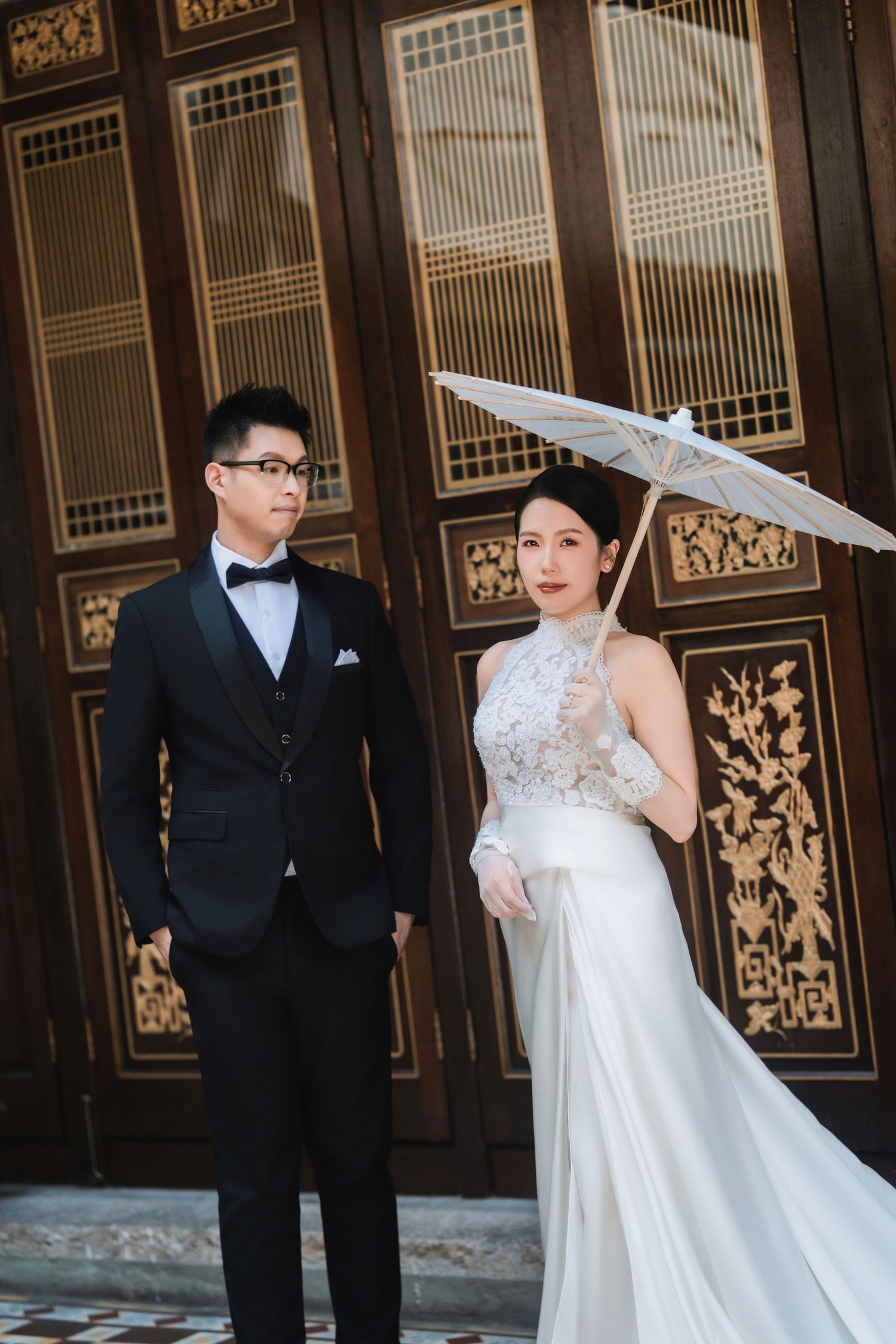 Wedding couple posing with parasols against ornate Asian architectural details.