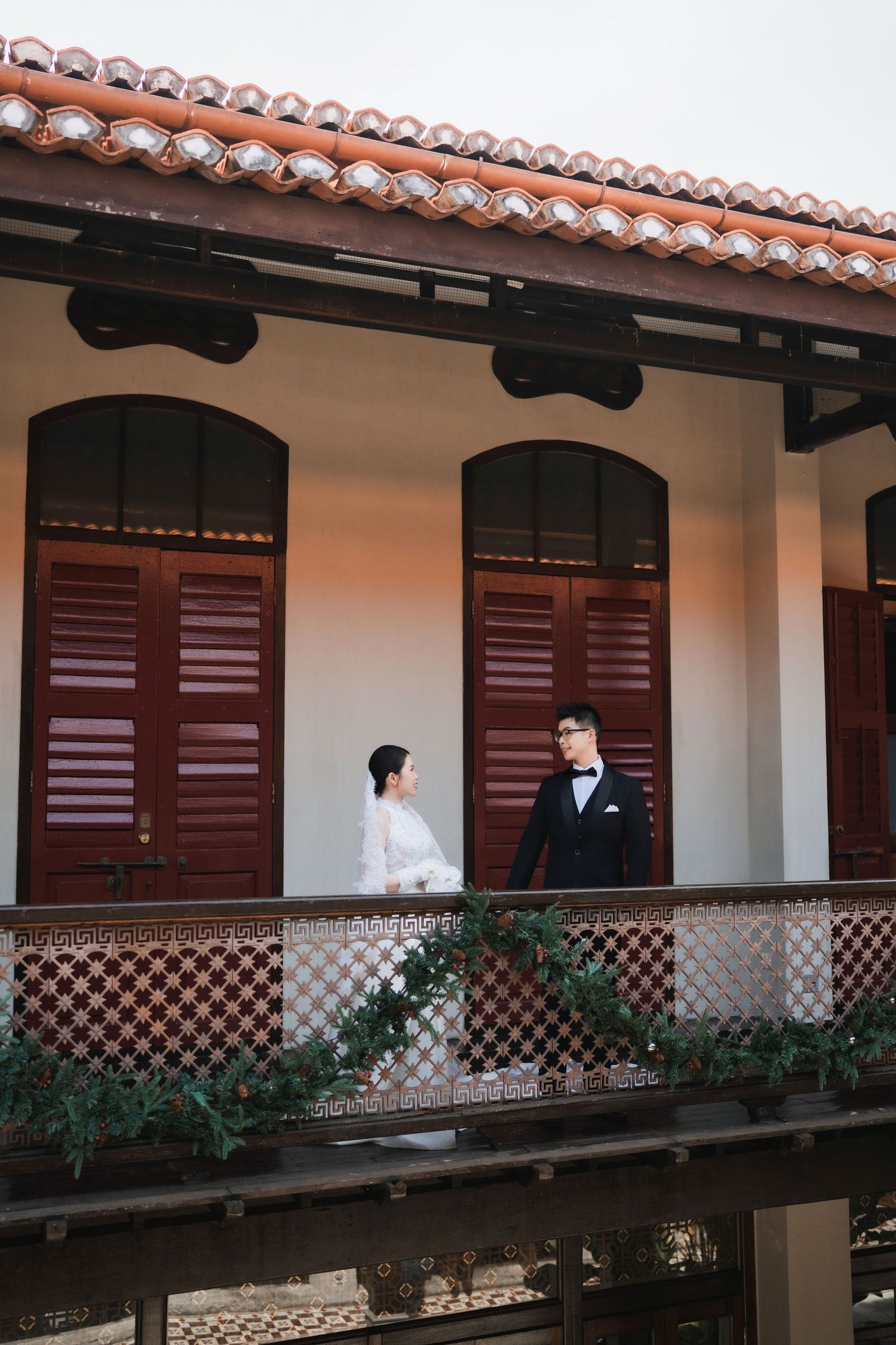 Wedding couple on traditional covered walkway with terracotta roof and white walls.