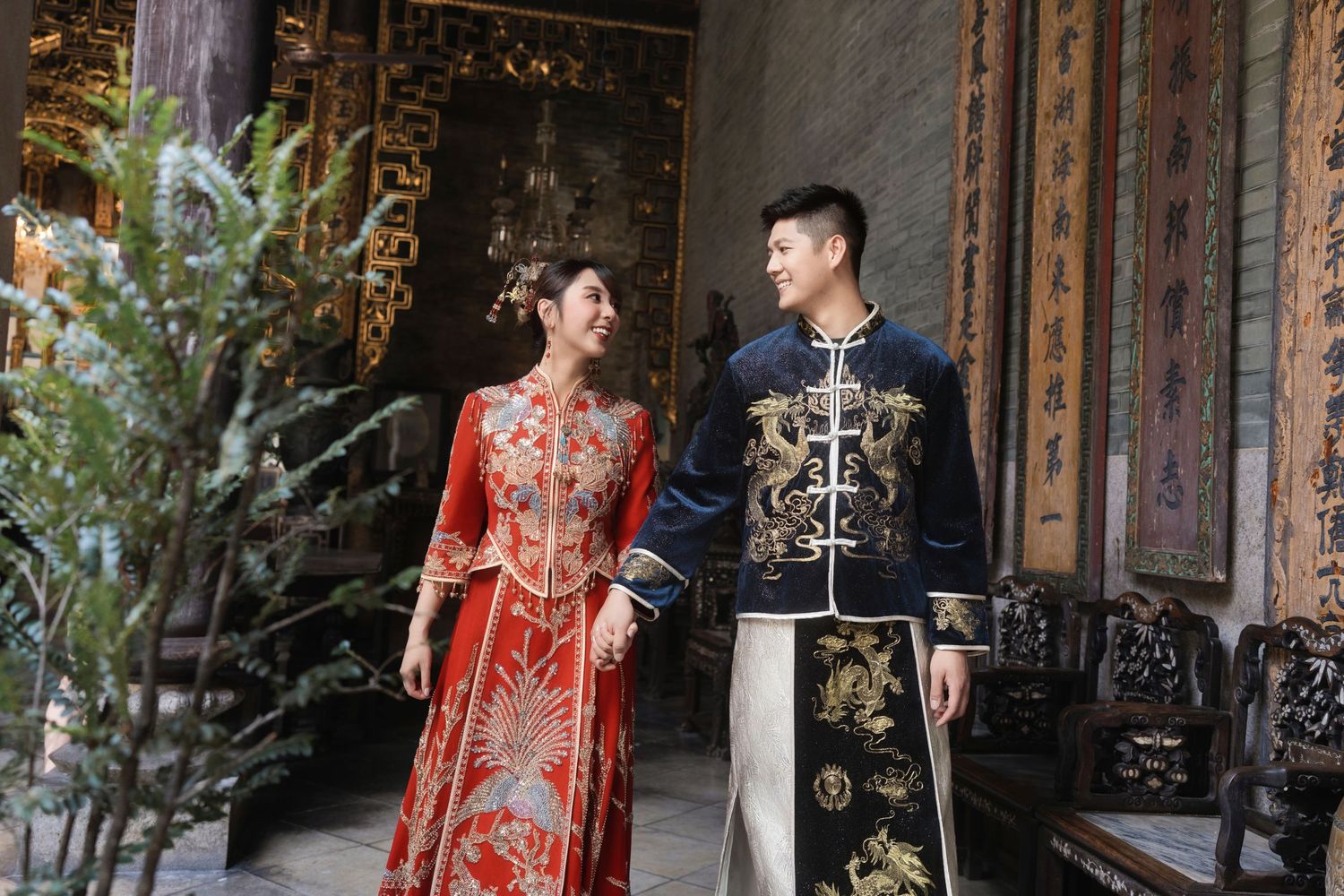 Couple in ornate Chinese wedding outfits walking through a traditional courtyard, showcasing cultural bridal fashion