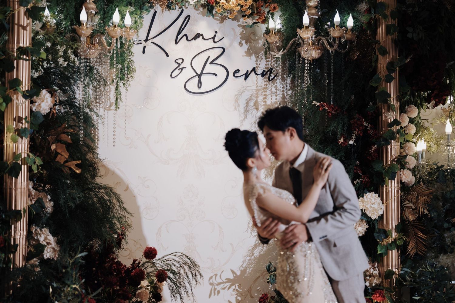 Newlyweds kissing before an elegant wedding photo backdrop decorated with cascading flowers and gold pillars