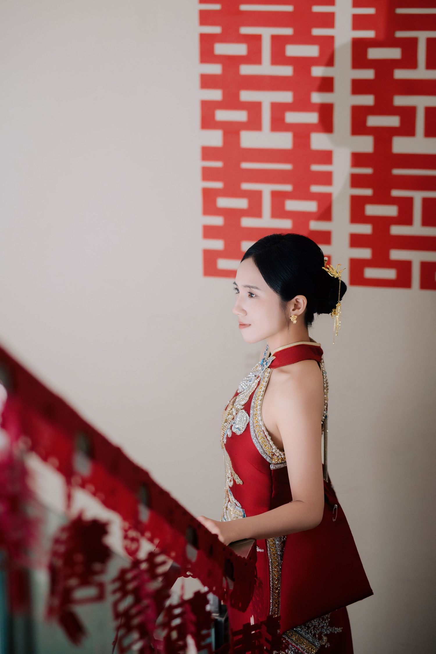 Profile view of the bride looking out from a staircase decorated with red Double Happiness paper cuts