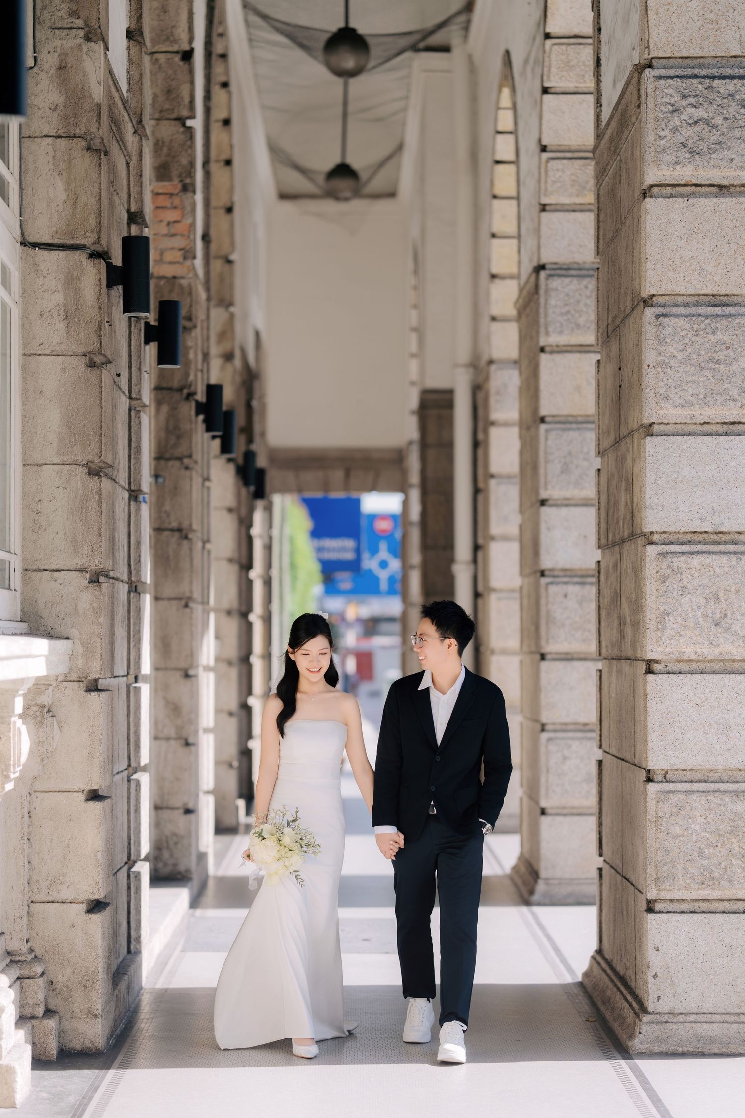 A couple walks through a classic colonnade hallway with stone pillars and arches.