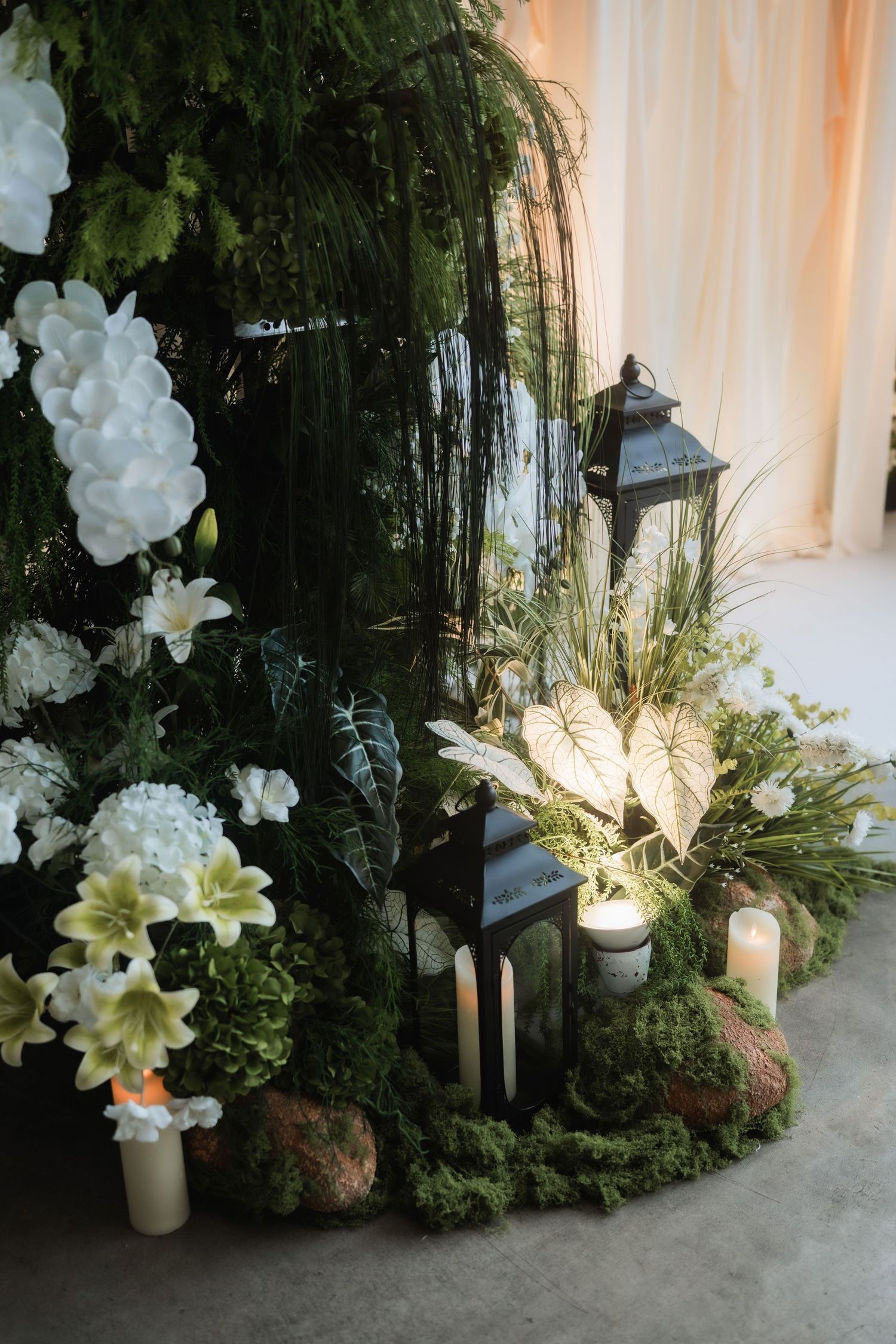 Wedding decor featuring white orchids and lush greenery with glowing candle accents.