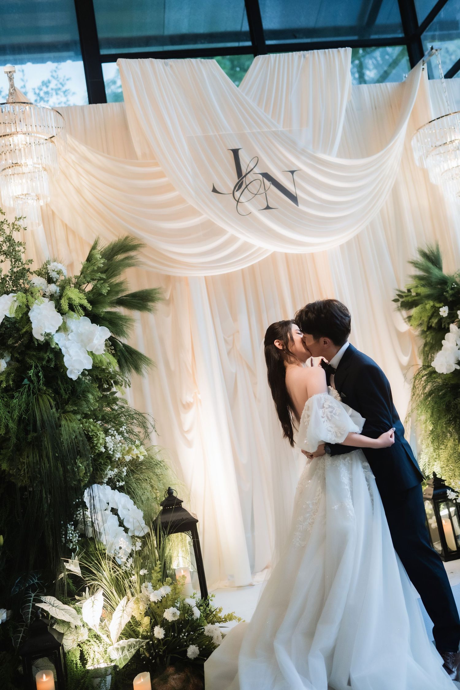 A romantic wedding ceremony moment under elegant white drapes and floral decorations.
