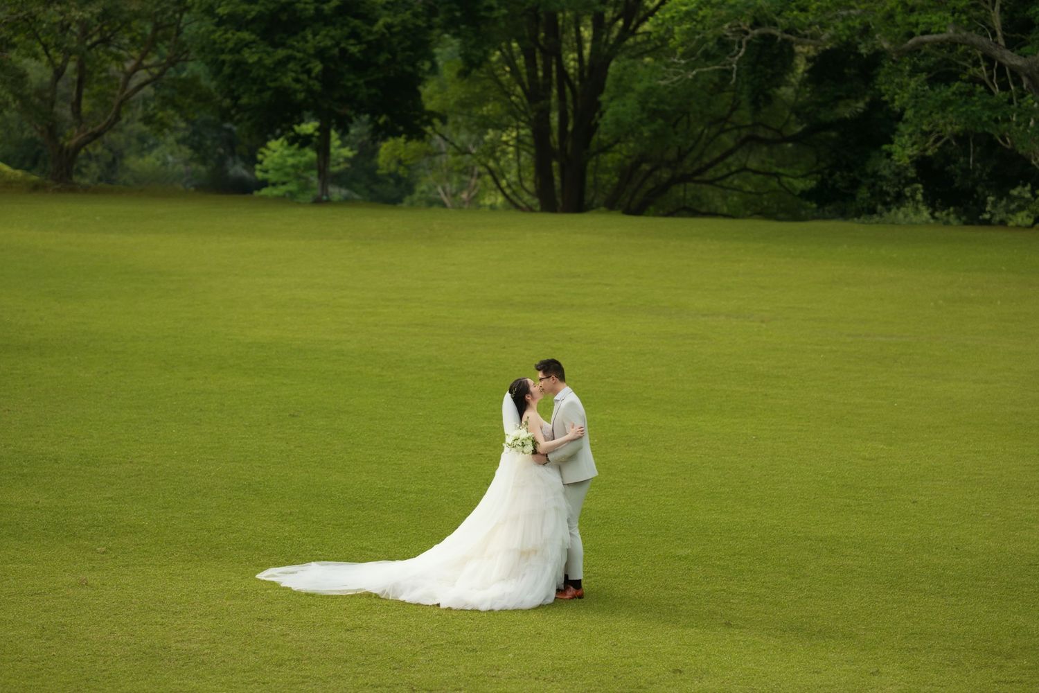 Romantic wedding portraits captured on a vast green lawn with trees in the background.