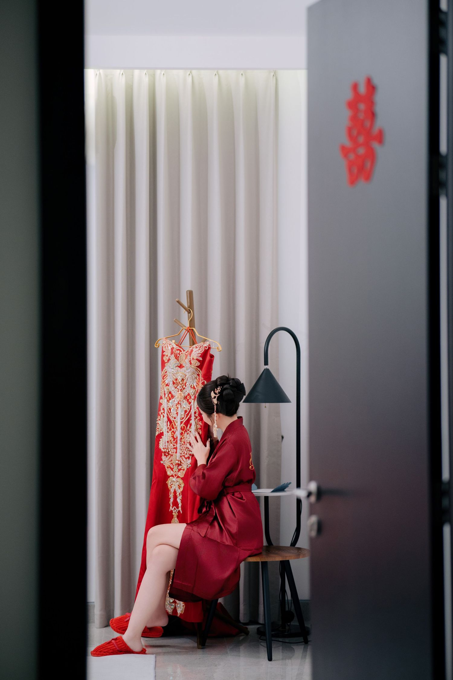 Traditional Chinese wedding preparation with red qipao dress in a minimalist dressing room.