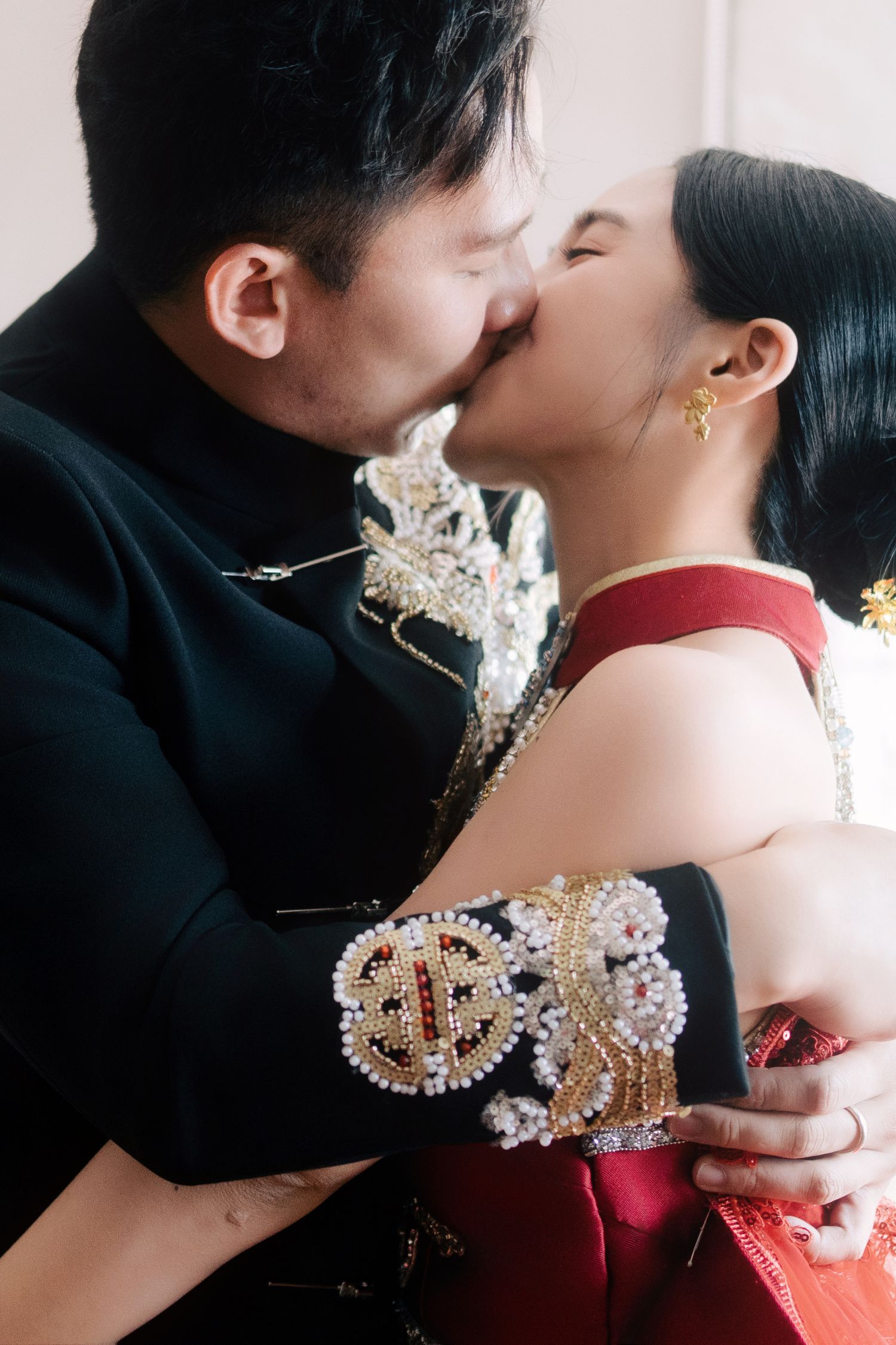Bride and groom kiss during their traditional Chinese wedding ceremony, wearing ornate silk wedding Kuas