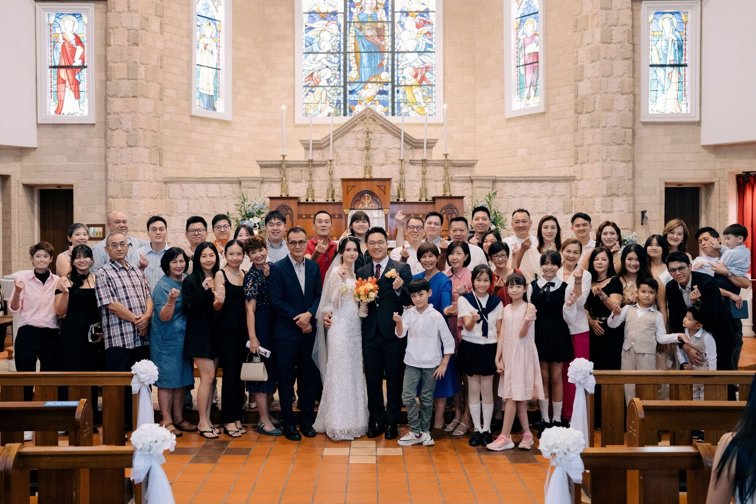 Large wedding party group photo at the altar of a Catholic church with stained glass windows