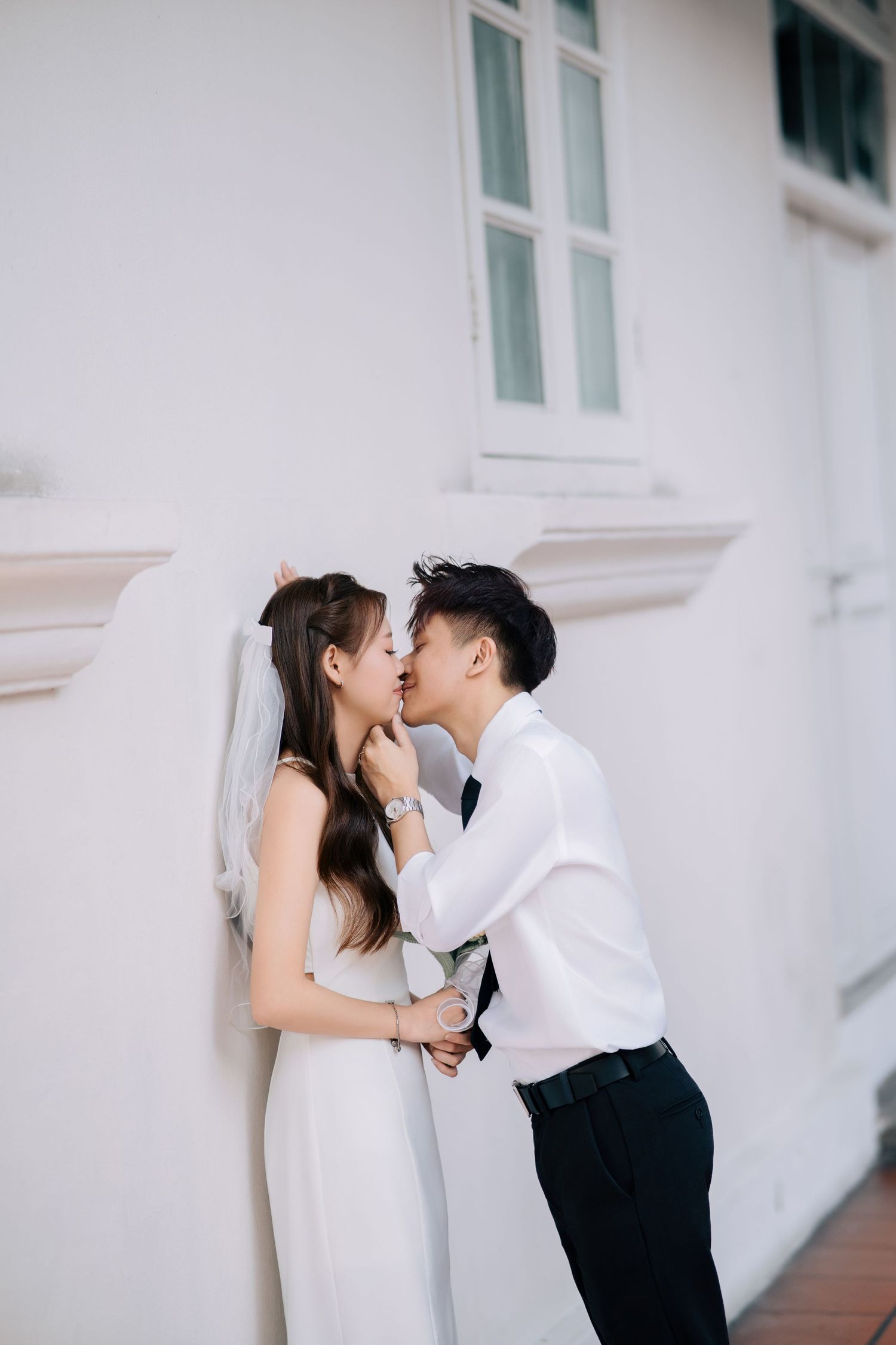A romantic couple shares a tender kiss against a white wall in an elegant wedding photoshoot sequence.