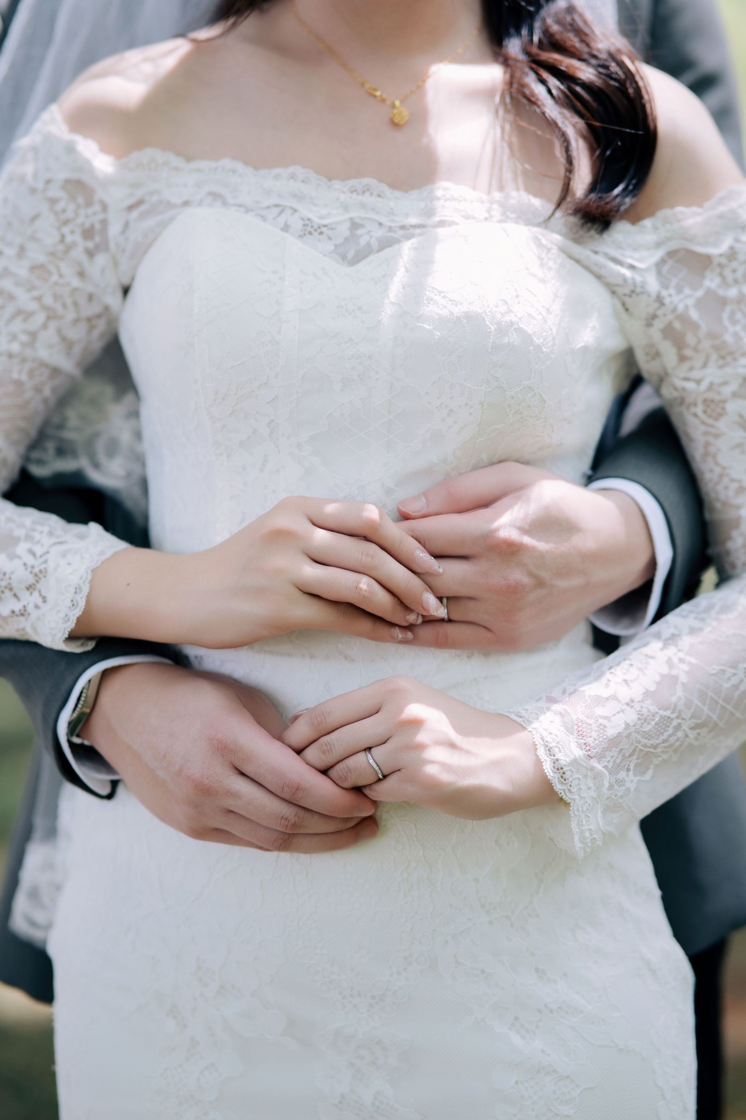 Close-up of wedding couple's hands showing rings and lace details.