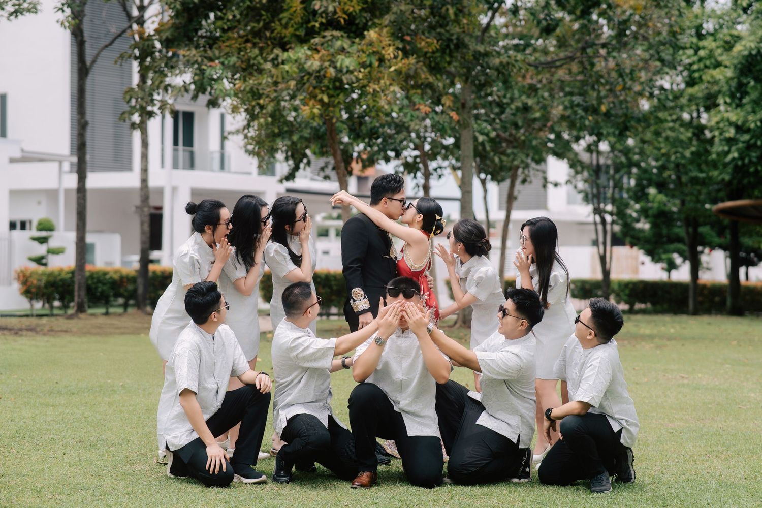 Bride and groom kissing while bridesmaids whisper and groomsmen cover their eyes or watch