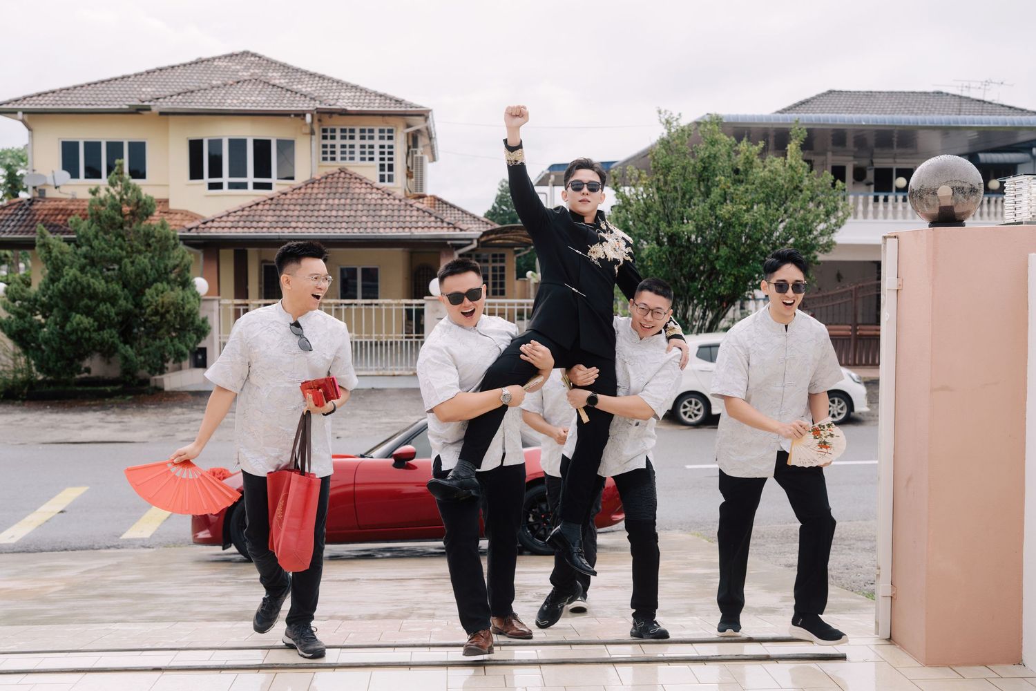 Groomsmen carrying the groom on their shoulders while walking and cheering toward a house