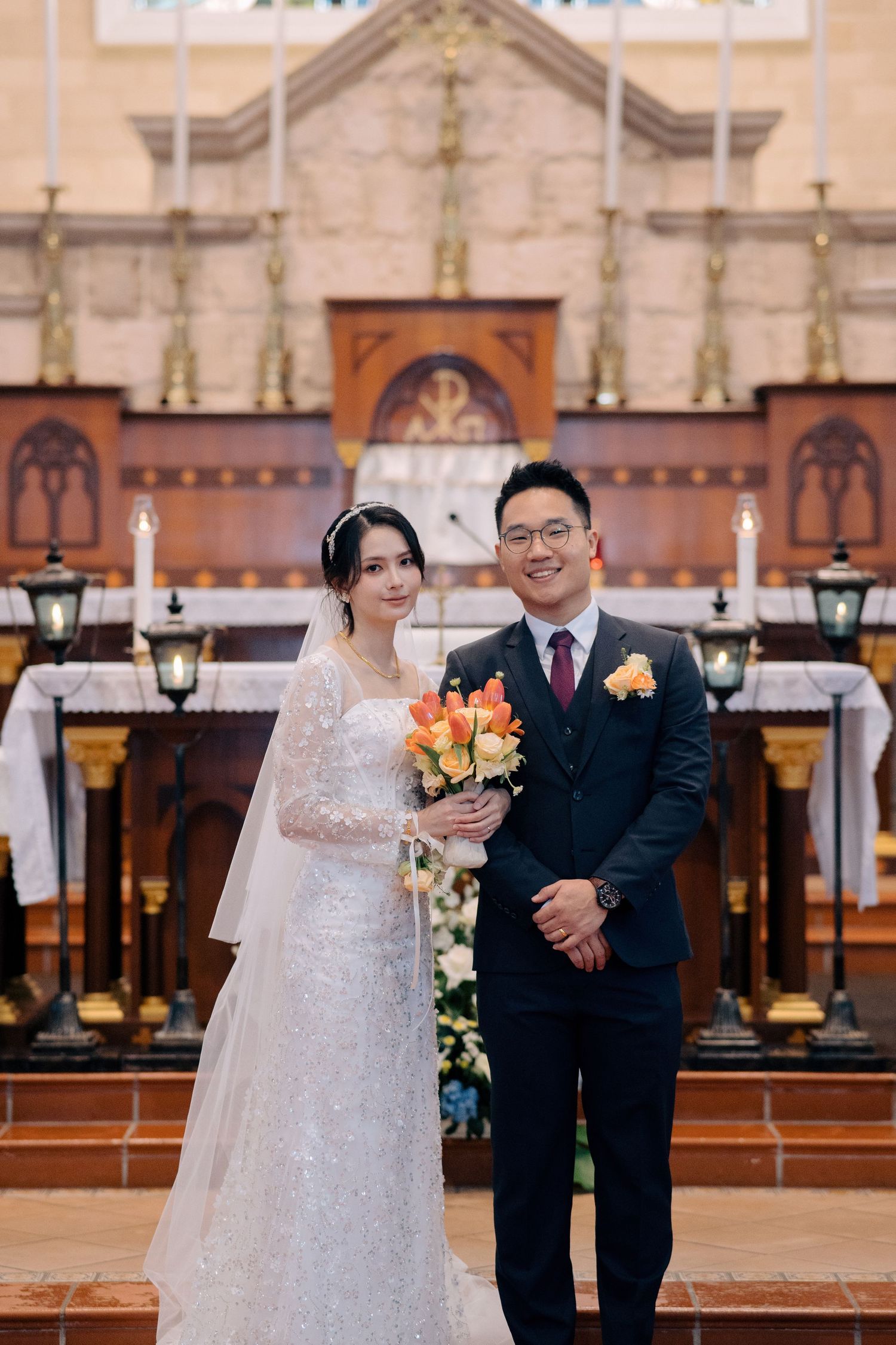 Bride and groom posing for a portrait in front of the altar during their Catholic wedding