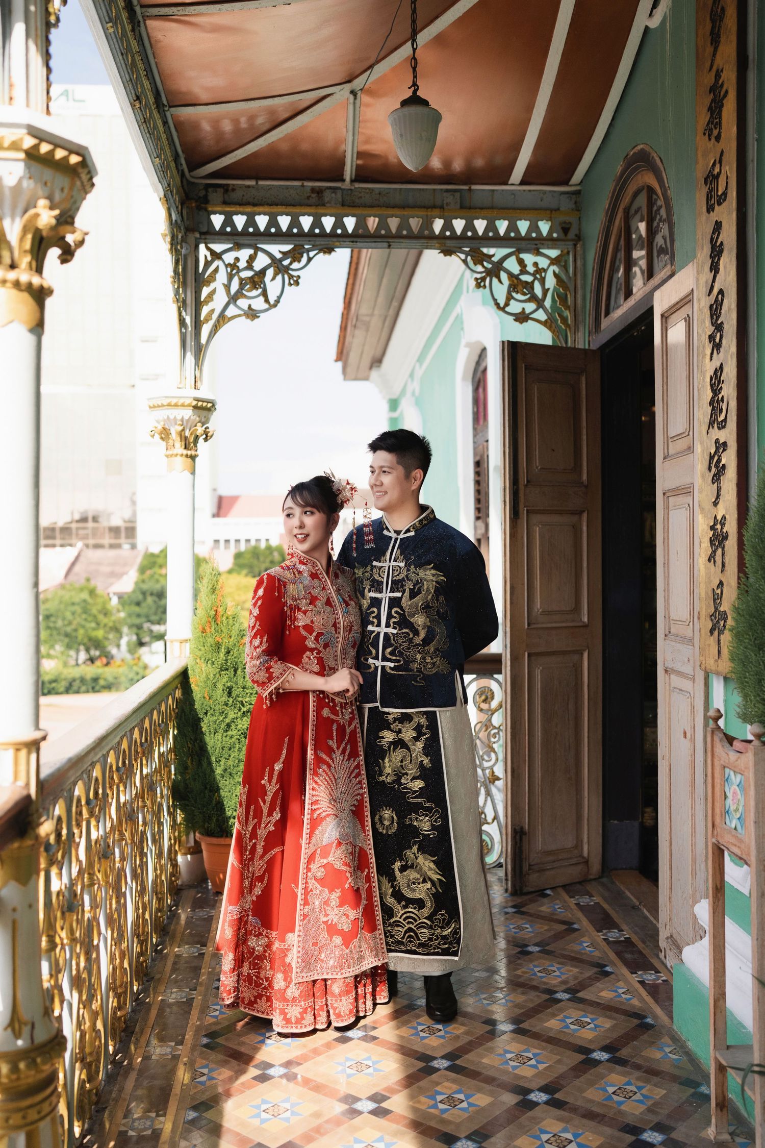 Couple posing for Peranakan wedding photography at a heritage mansion wearing a traditional red Kua and navy dragon robe
