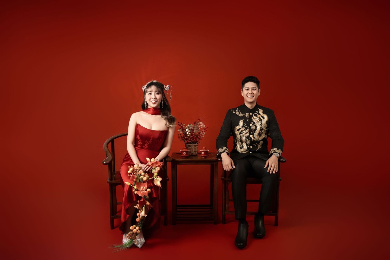 Studio wedding portraits with traditional Chinese elements against vibrant red background.