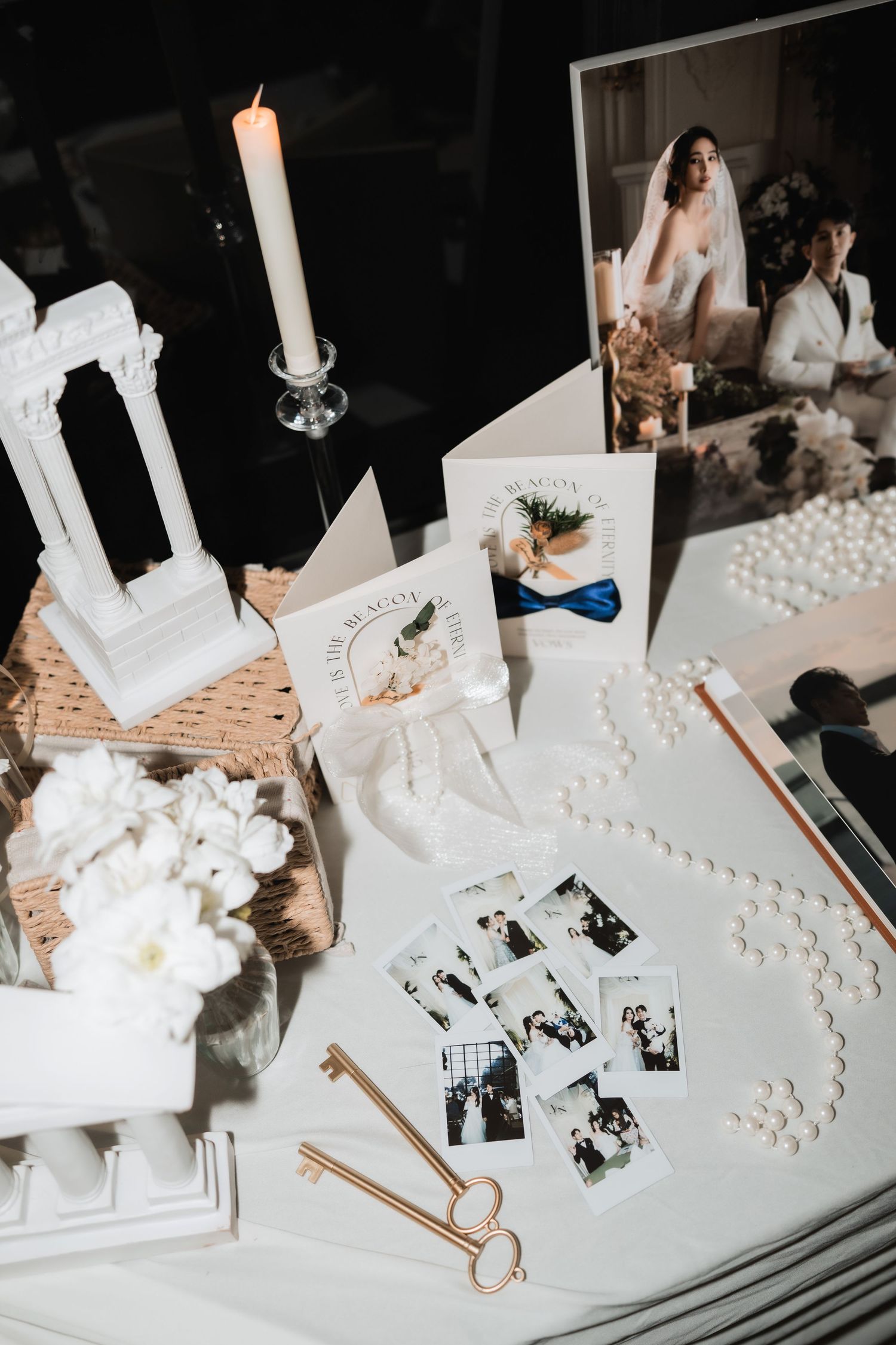 Wedding table details with white candles, pearls, and photographs arranged on a decorative surface.