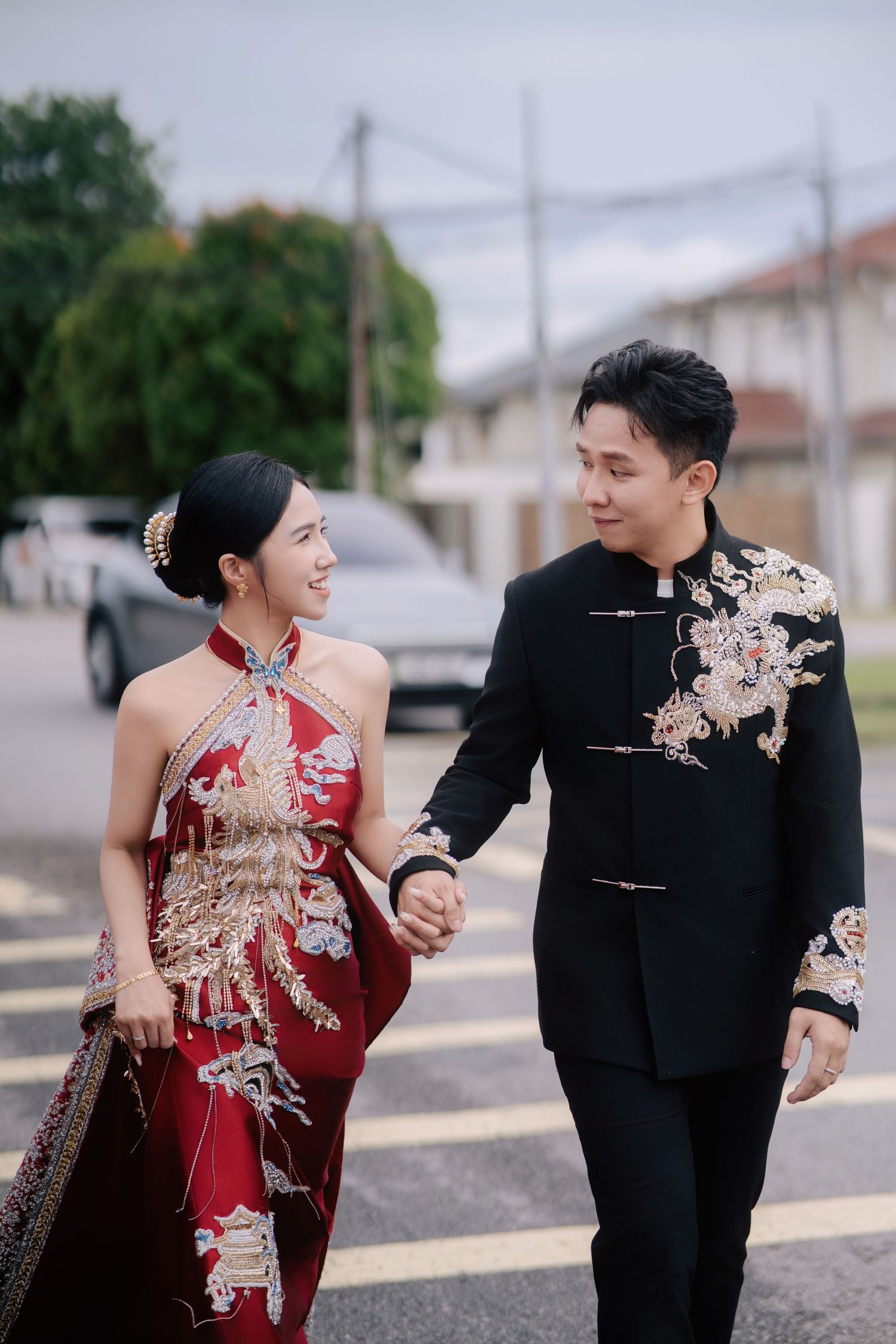 Bride smiles and lifts her dress while holding the groom's hand as they walk across a paved street