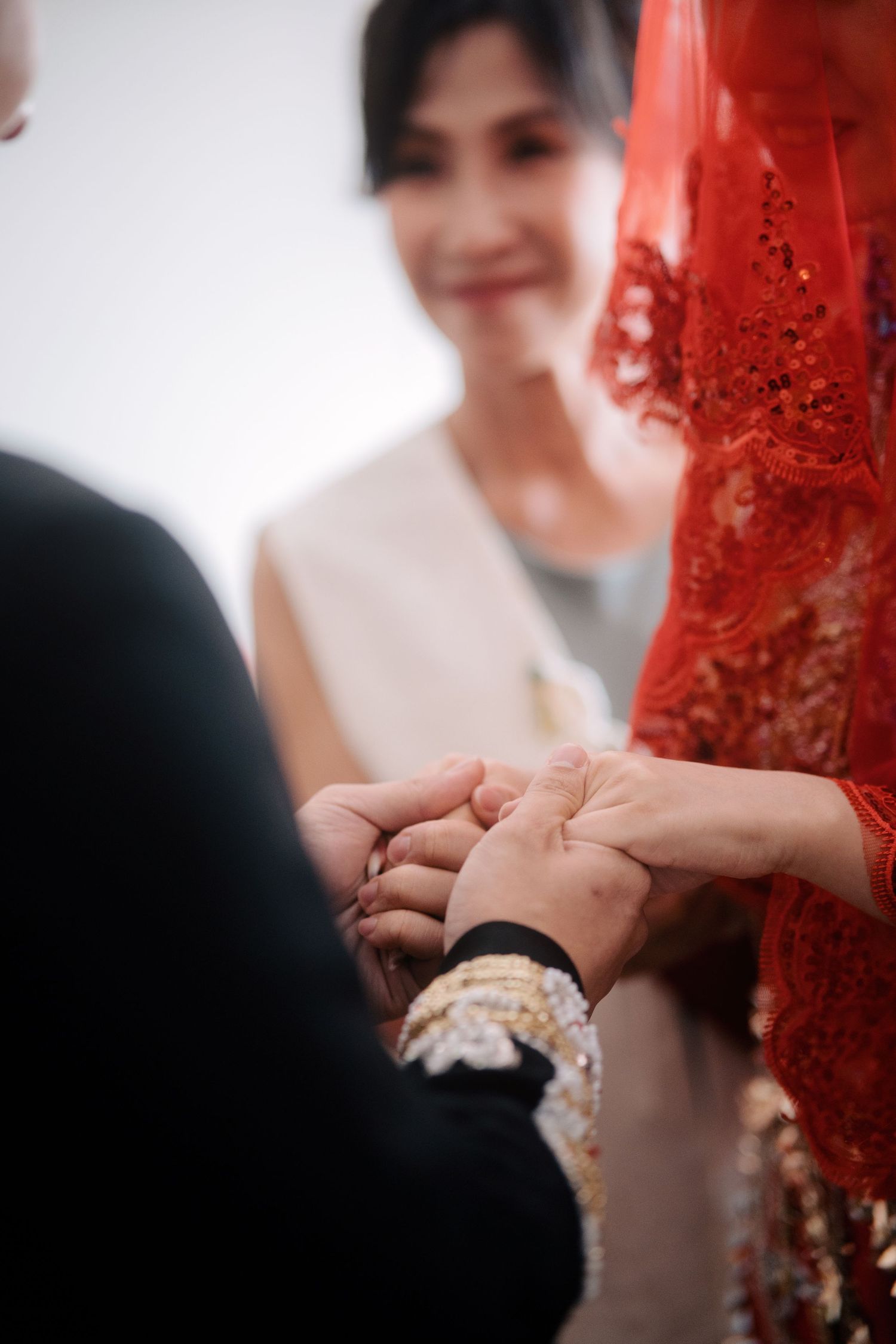 Detail of groom and bride holding hands, showcasing ornate embroidery of traditional Chinese wedding garments