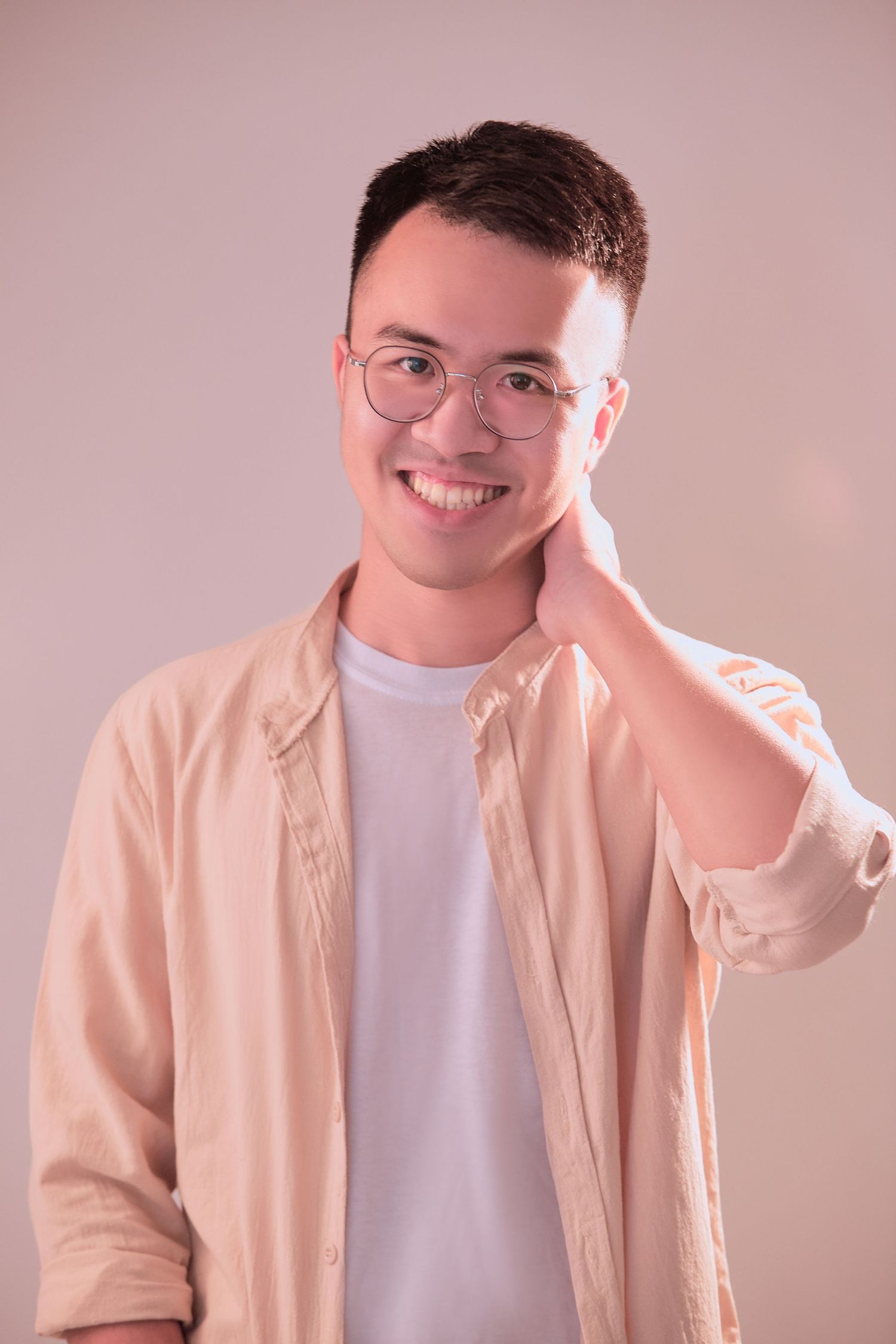 Person wearing glasses and light pink button-up shirt over white t-shirt poses against pink background.