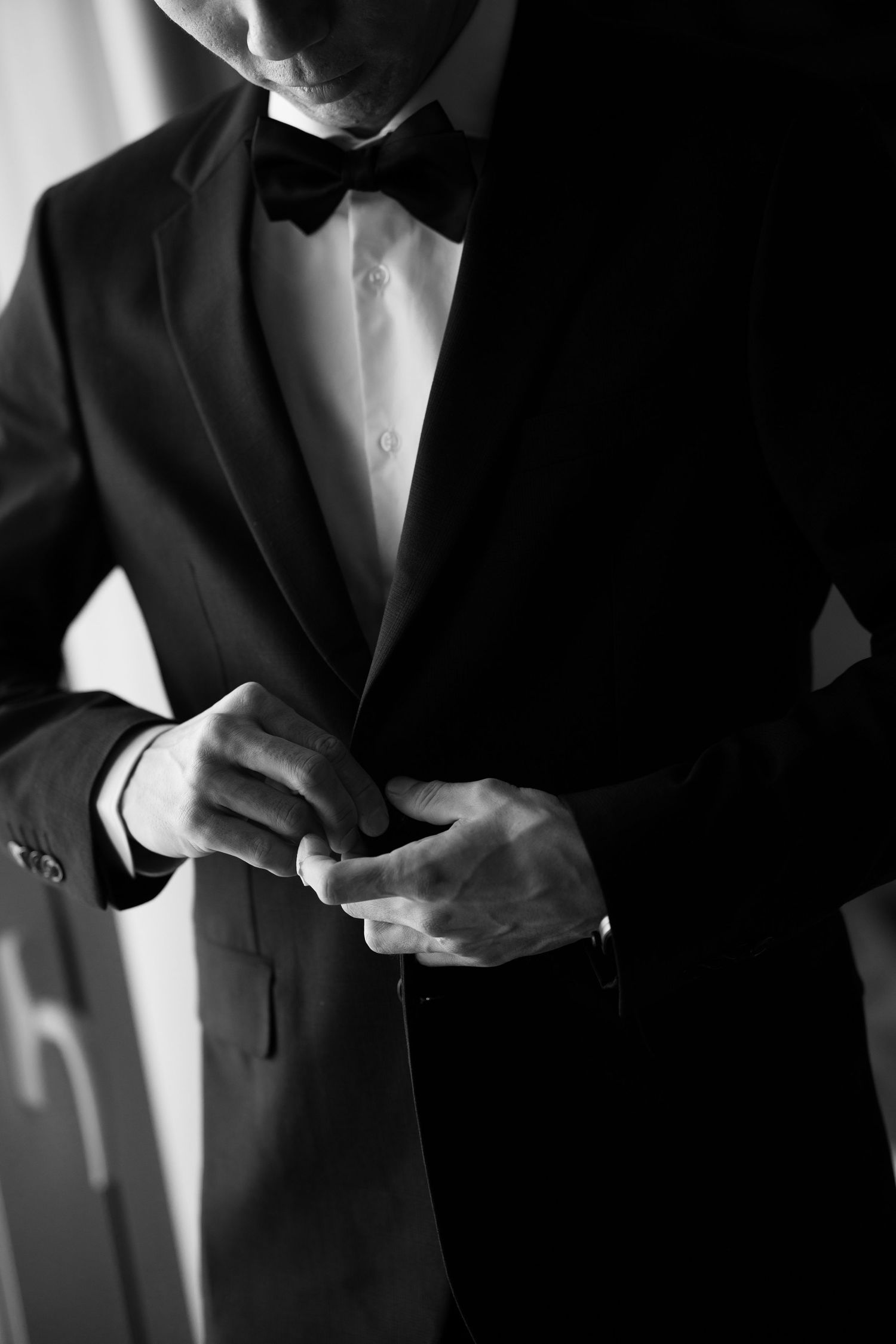 Close-up black and white photo of hands adjusting bowtie on formal tuxedo.