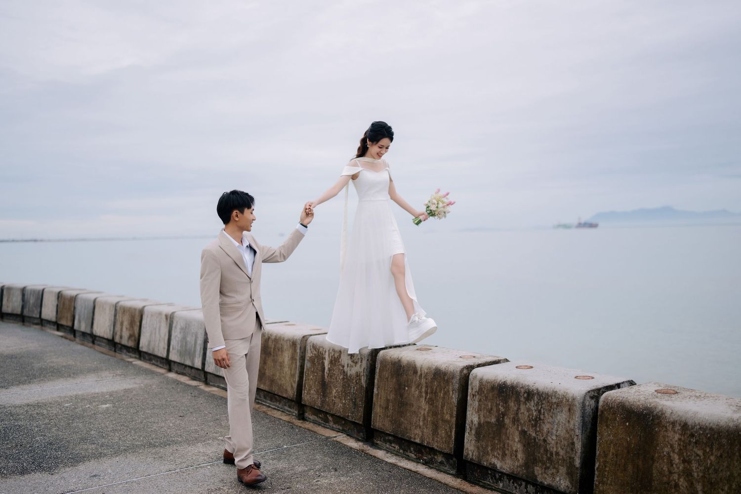 Playful wedding photography session along concrete seawall with ocean view.