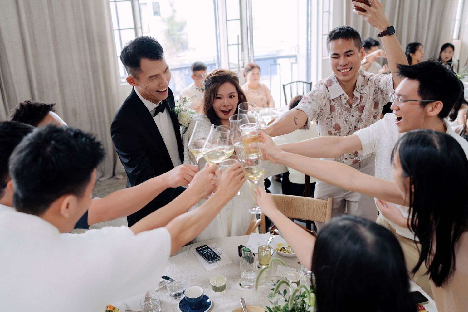 Group of friends and the wedding couple clink wine and beer glasses over a dinner table