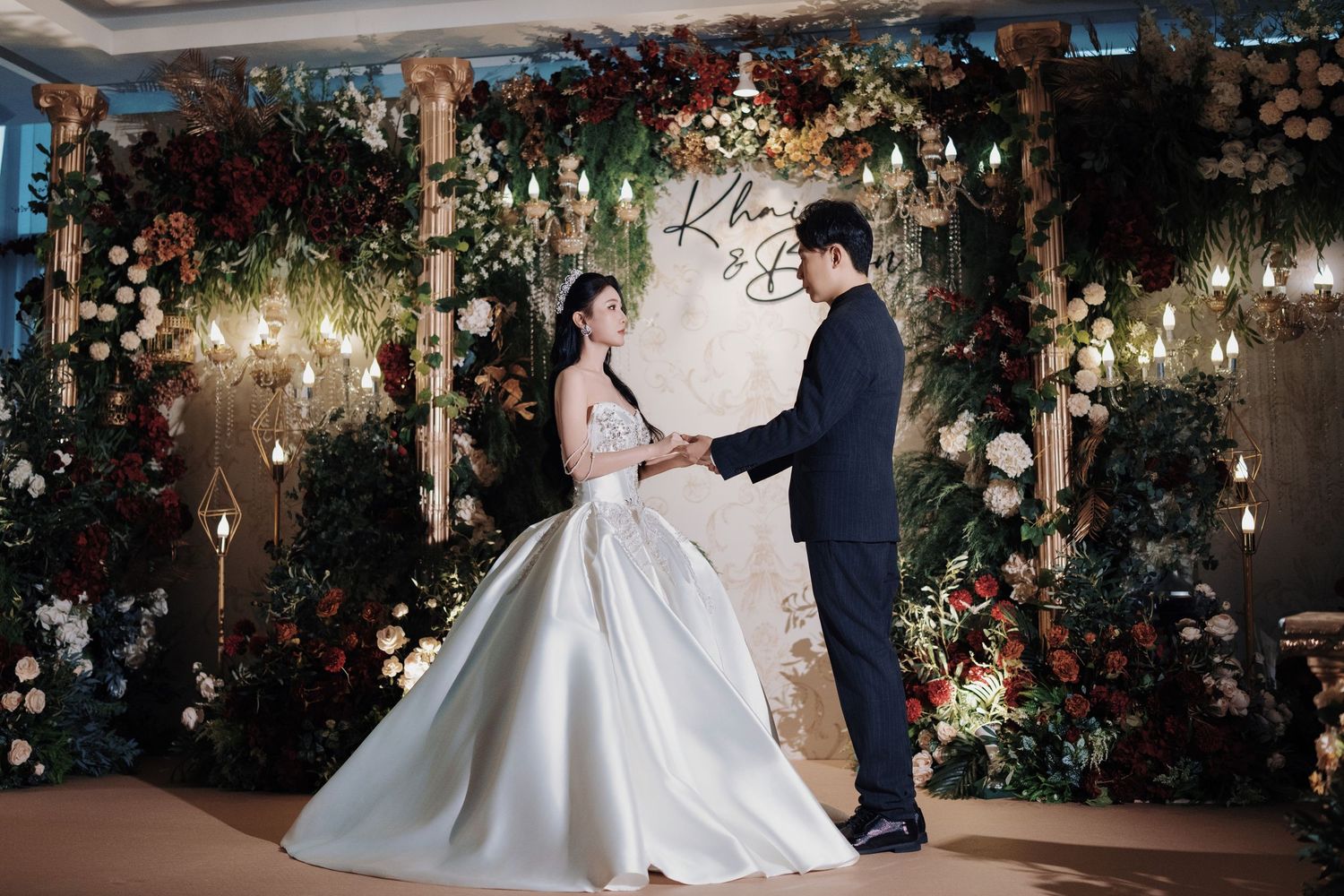 Bride and groom holding hands at the altar, surrounded by lush greenery and romantic red florals