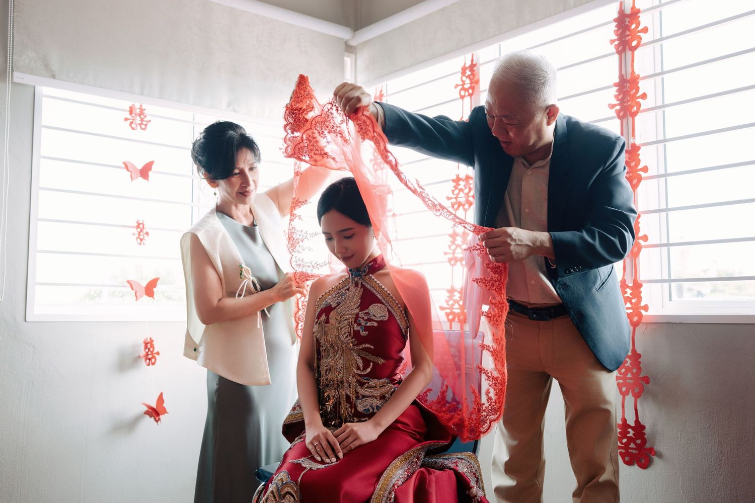Parents gently placing a red bridal veil over their daughter during a traditional Chinese wedding in Penang