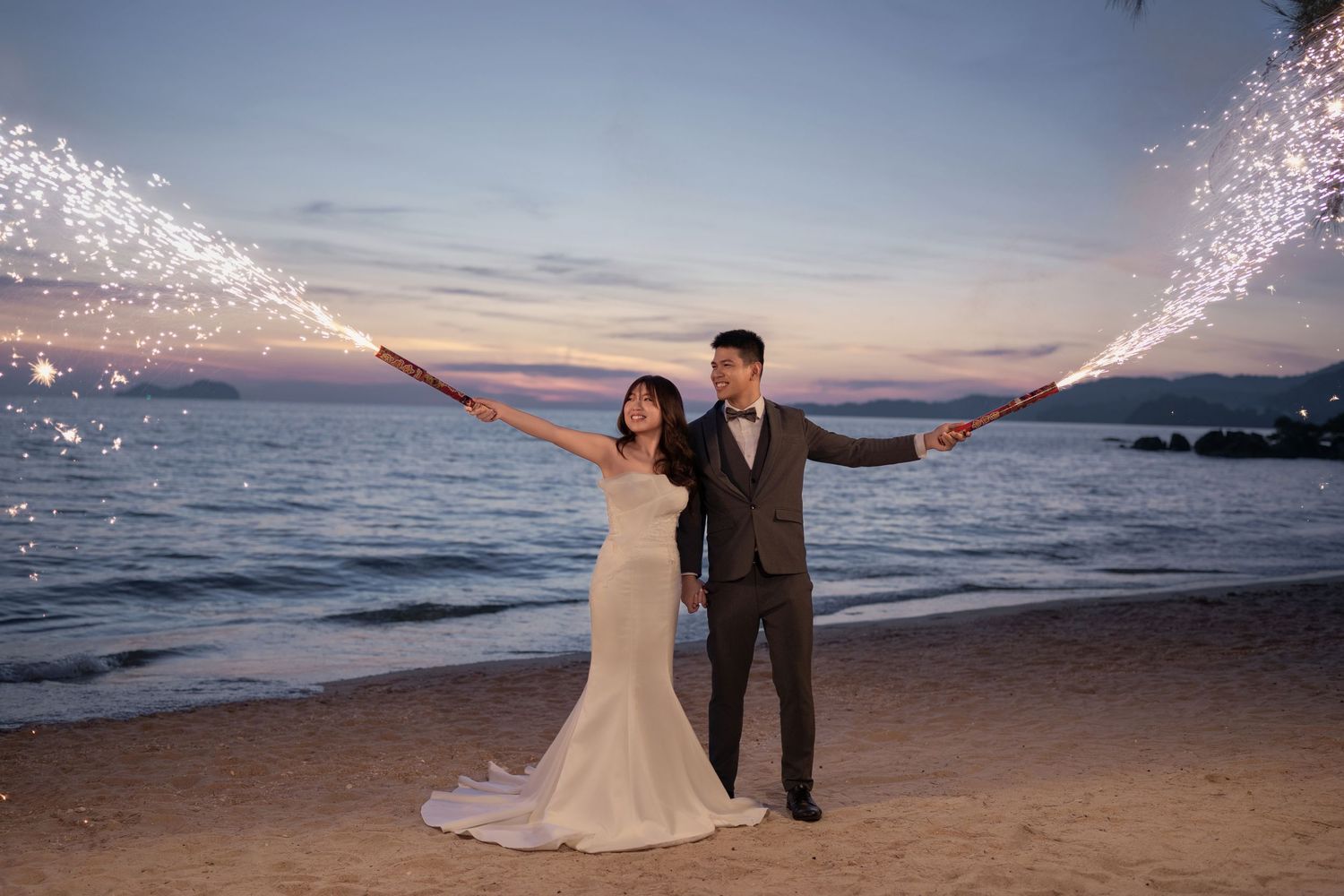 Sparklers illuminate a beachside wedding photoshoot during golden hour.
