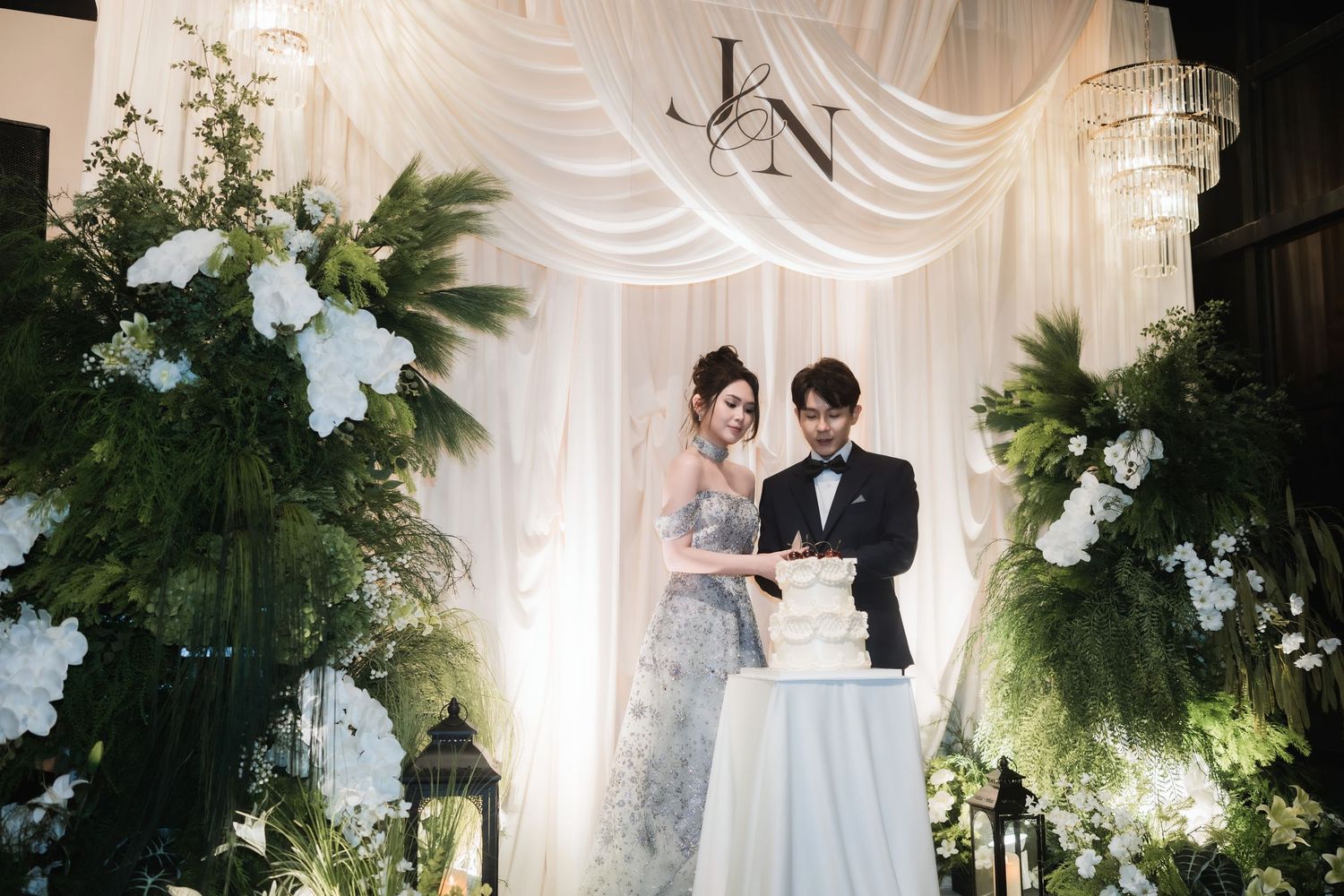 An elegant wedding ceremony setup with white drapes and green floral arrangements.