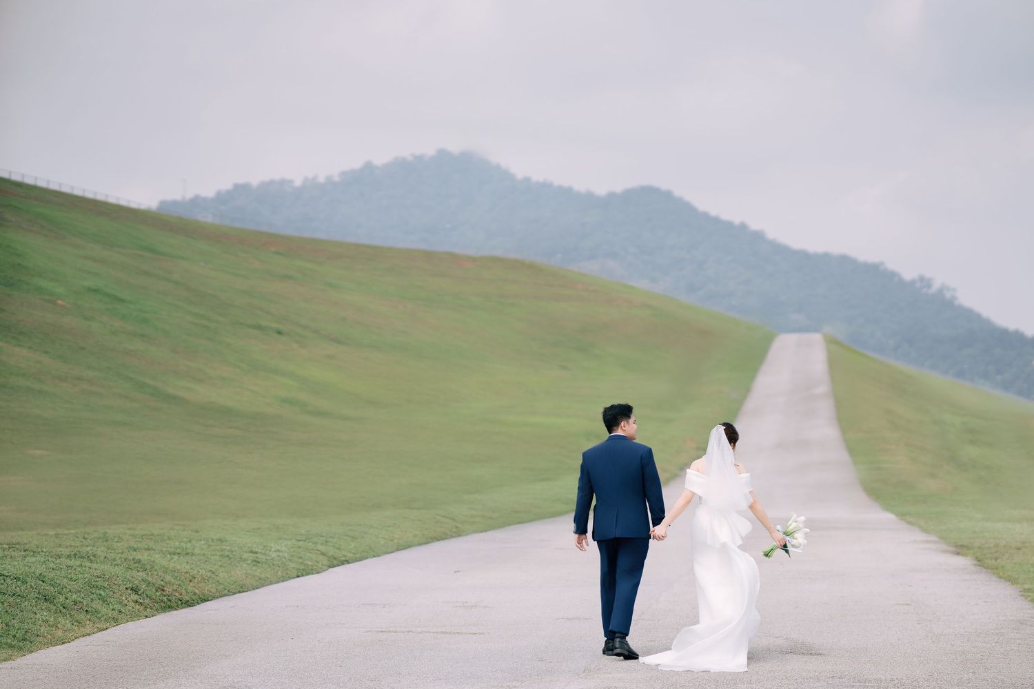A couple walks down a long winding road through green rolling hills.