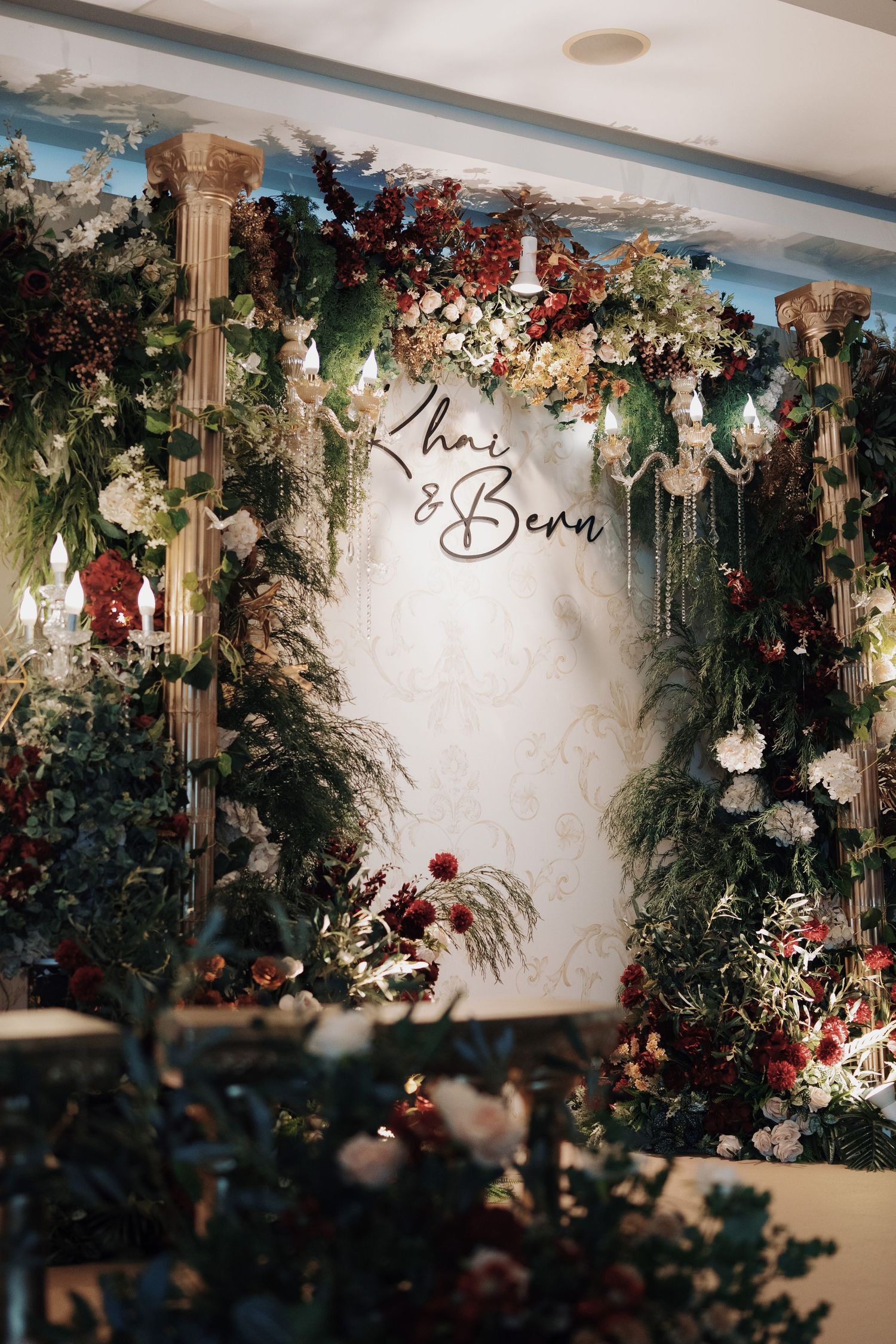 Enchanted forest wedding decor featuring floral backdrop, crystal chandeliers, and custom couple monogram