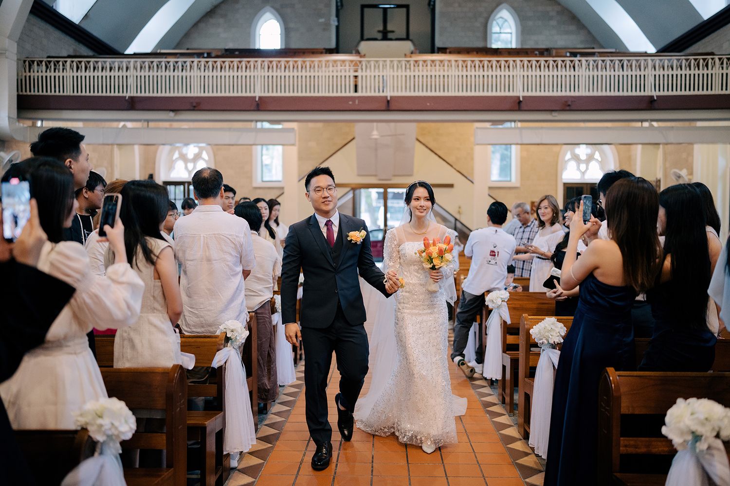 A bride in a sparkling lace dress and a groom in a suit walking together through a wedding congregation