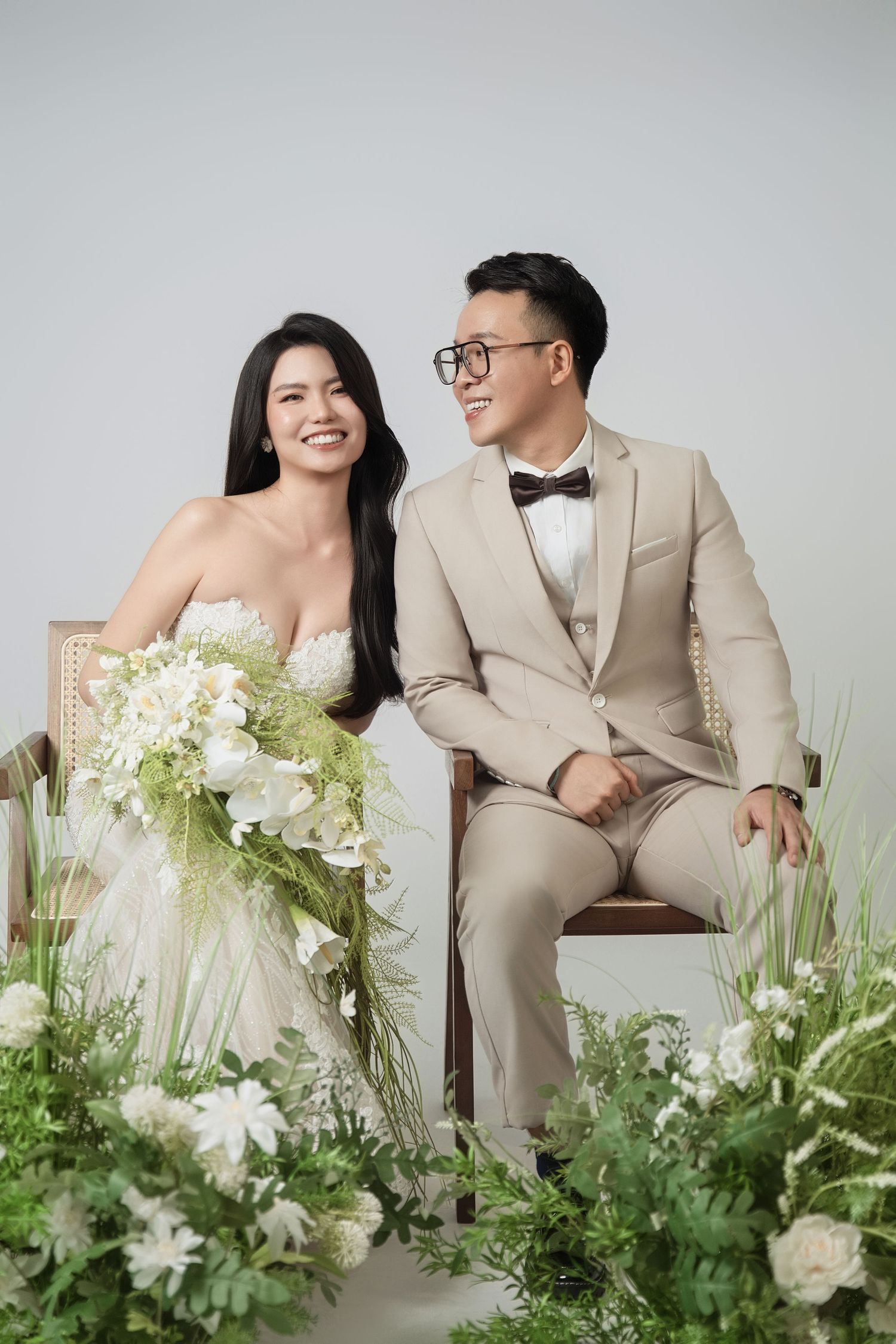 Elegant wedding photo shoot with white floral arrangements and a beige suit against a light background.