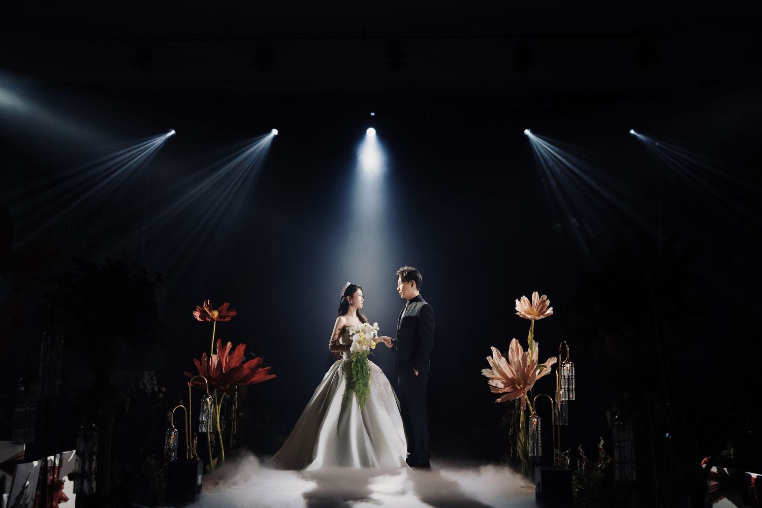Dramatic wedding scene with spotlights and floral decor on a misty stage during an evening celebration at Olive Tree Hotel's Grand Ballroom.