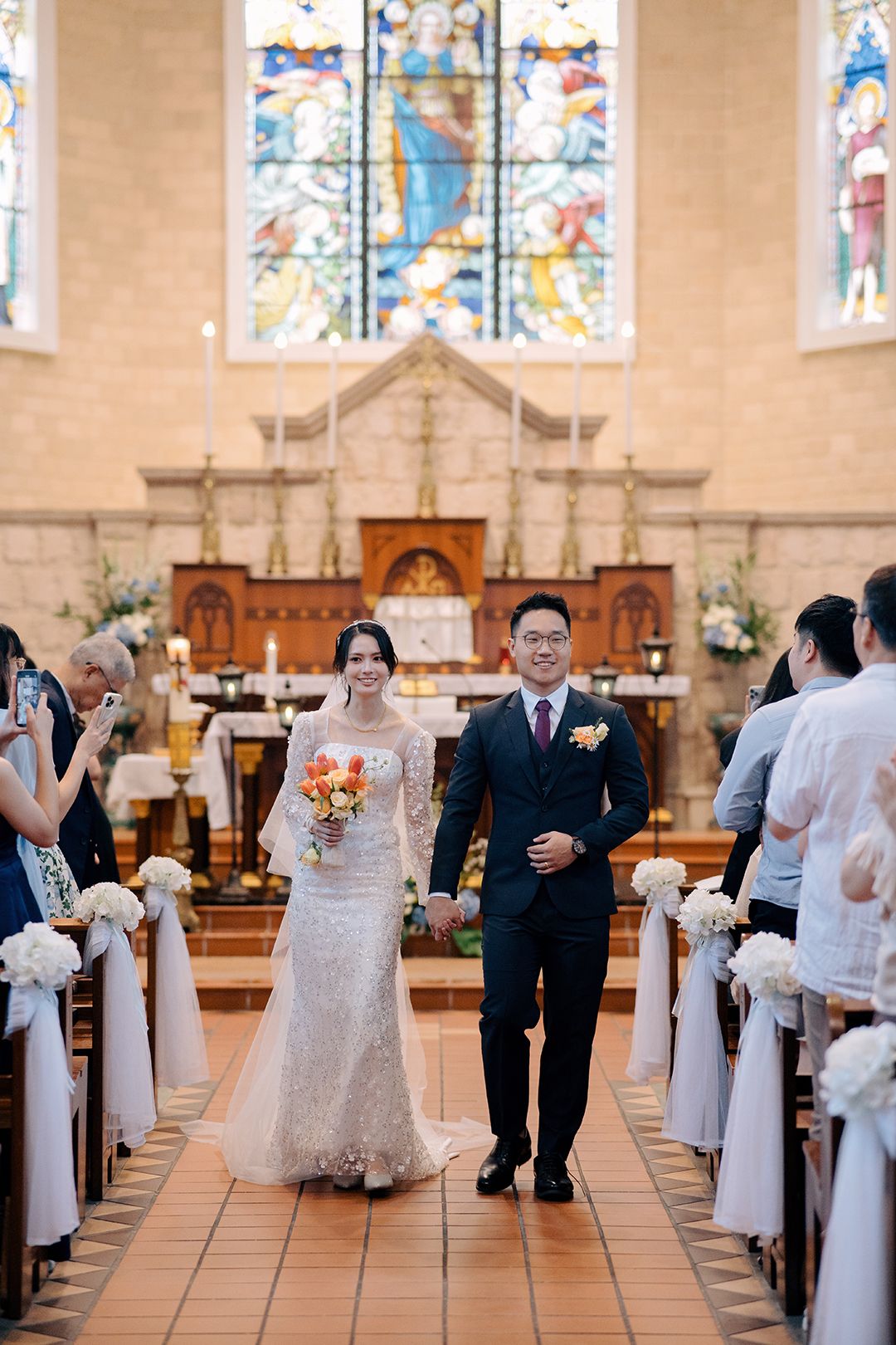 Newlyweds walking down the aisle after a Catholic church wedding ceremony with orange tulip bouquet