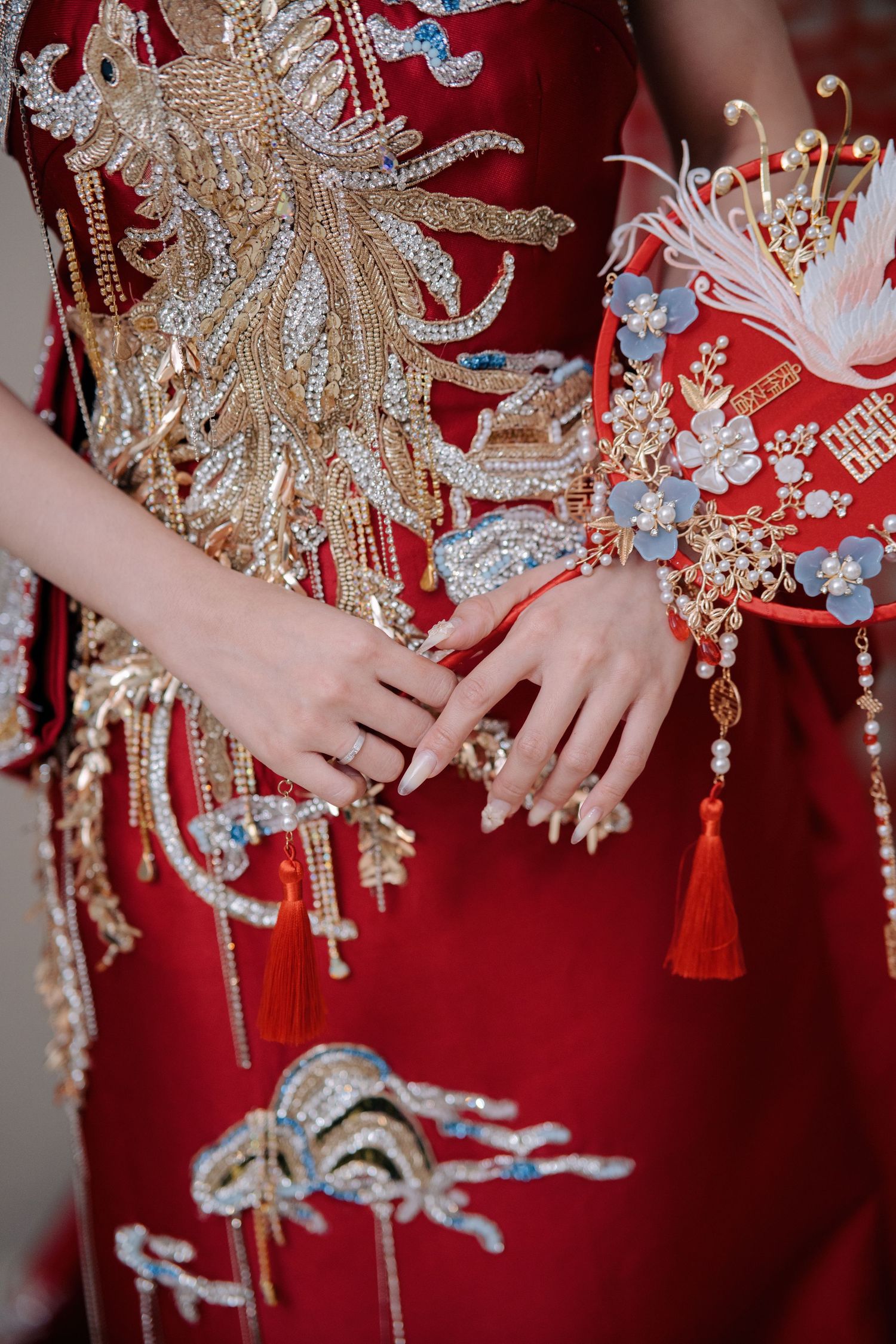 Bride holding a red silk wedding fan featuring intricate floral beadwork and traditional Chinese symbols