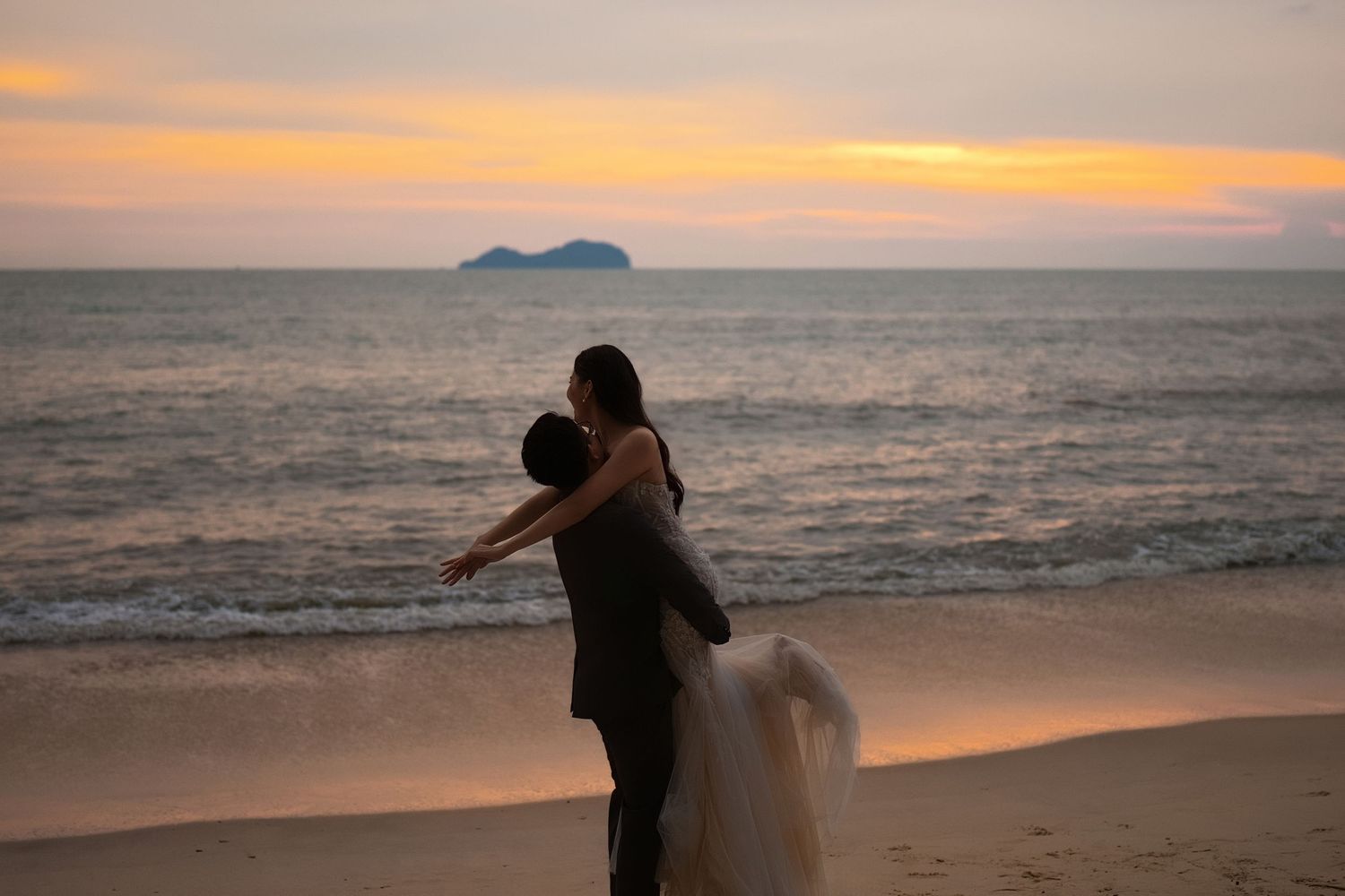 Romantic wedding photoshoot at Teluk Bayu Beach sunset featuring a groom lifting his bride on the sandy shore