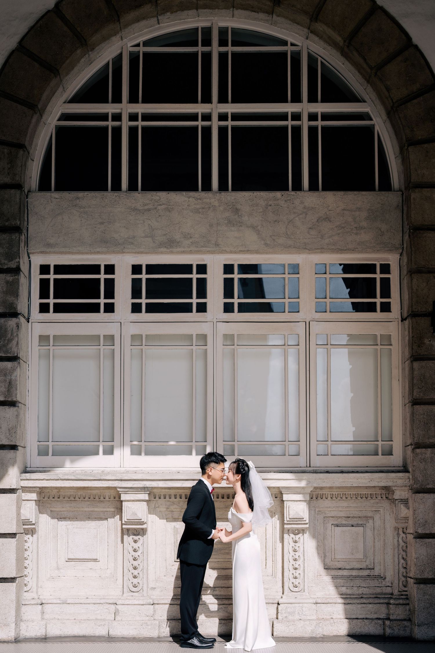 Heritage wedding photography featuring a bride in a minimalist gown and groom in a black suit by a historic arch