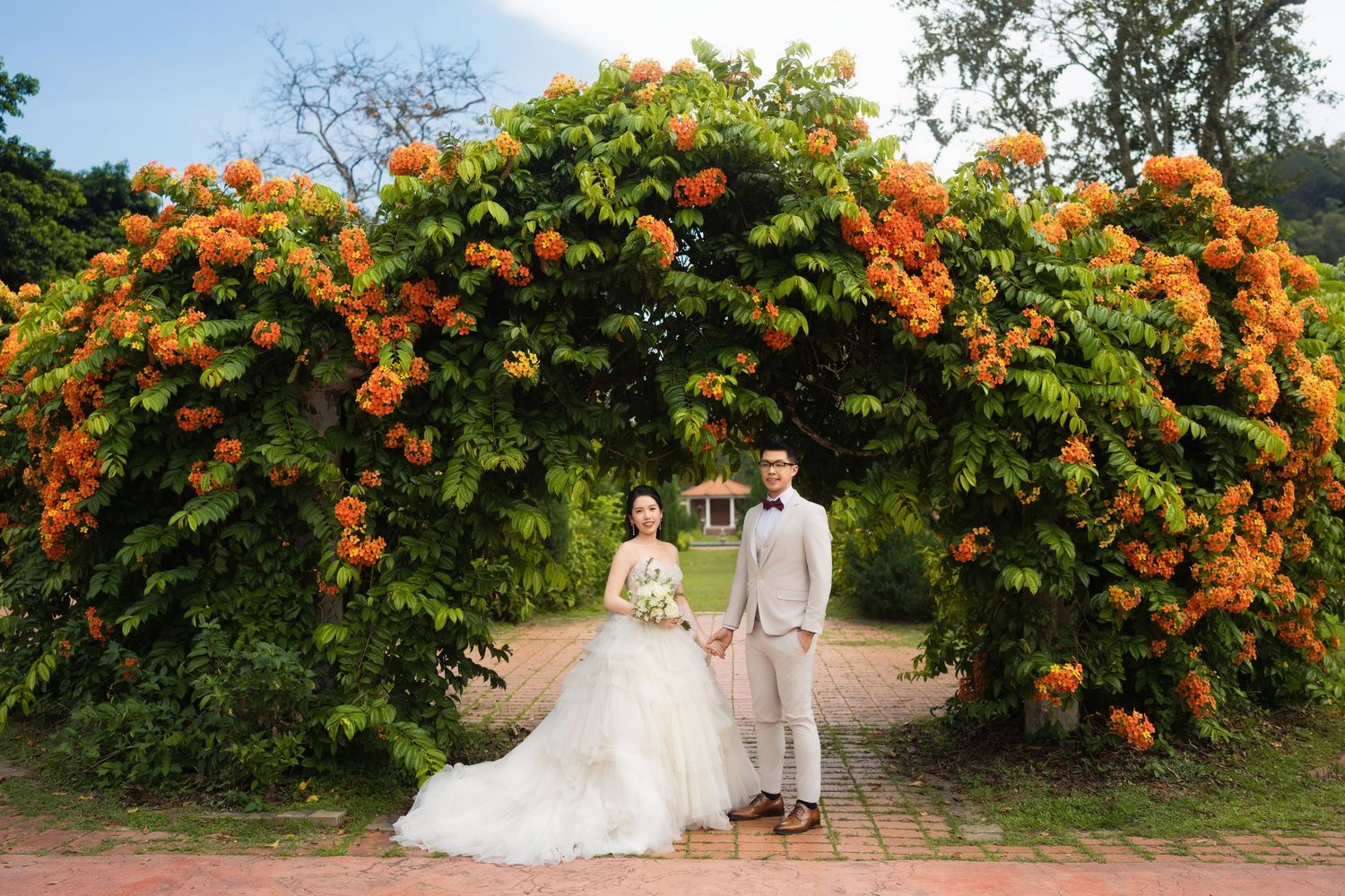 Bride and groom posing for a botanical garden wedding photo under a blooming orange floral canopy