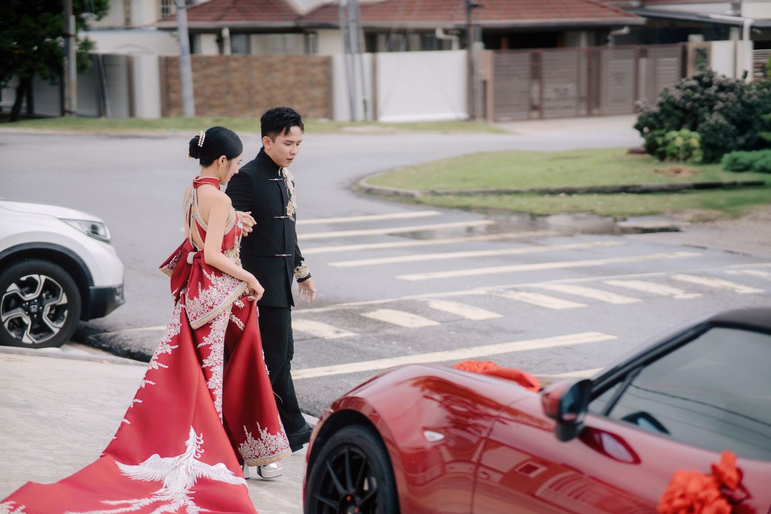 Bride in a red phoenix gown approaches the decorated car at a Traditional Chinese Wedding