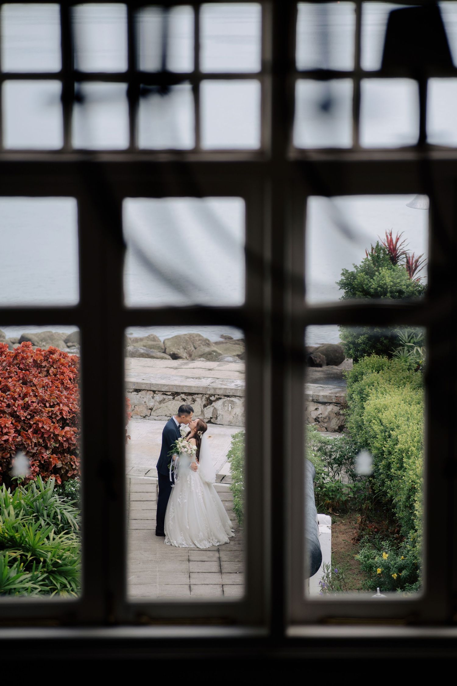 Wedding scene framed through window showing couple in garden setting at Eastern & Oriental Hotel (E&O).