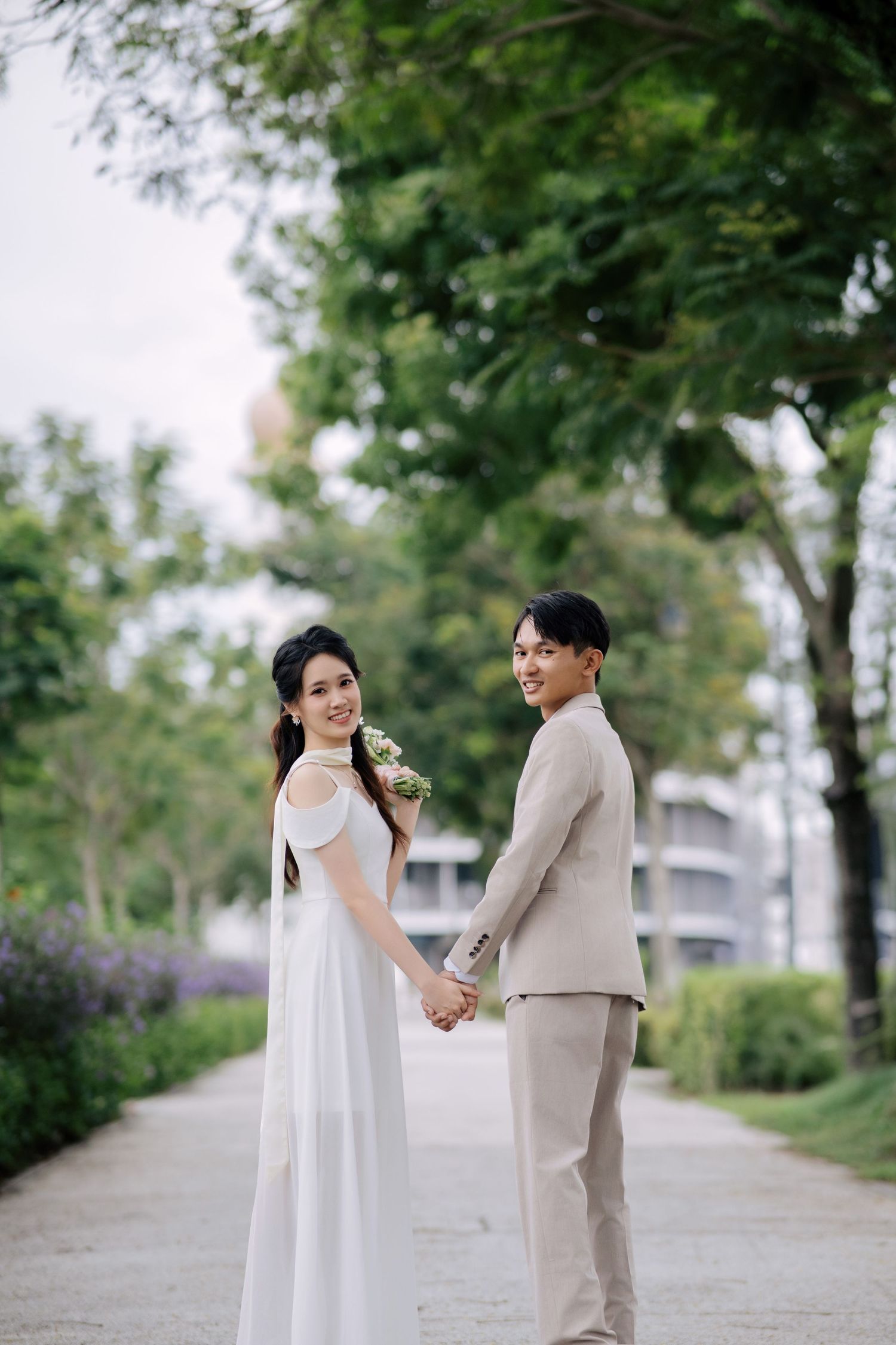 A couple holds hands on a garden pathway surrounded by lush greenery.