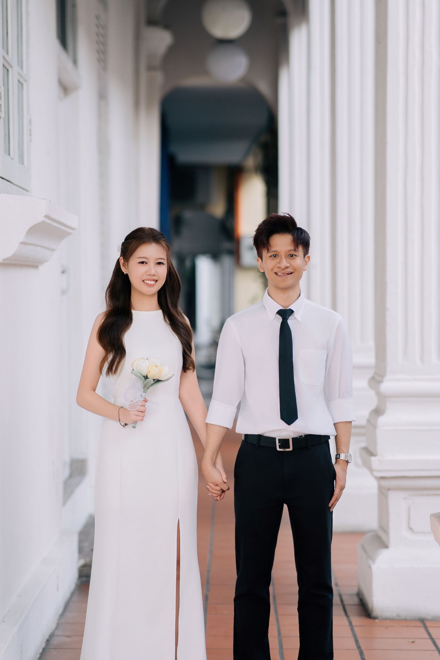 Couple in wedding attire poses together in front of white colonial columns.