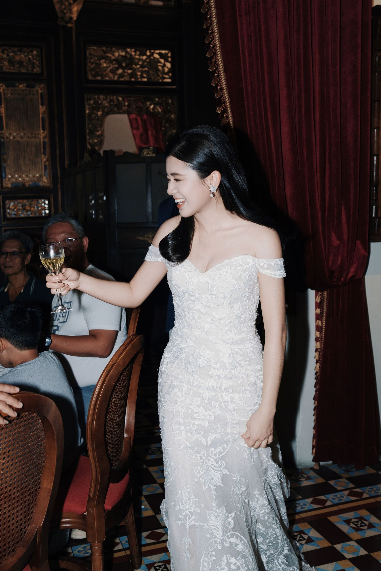 Bride in a white lace dress cheering with a glass of wine at Kebaya Dining Room Penang