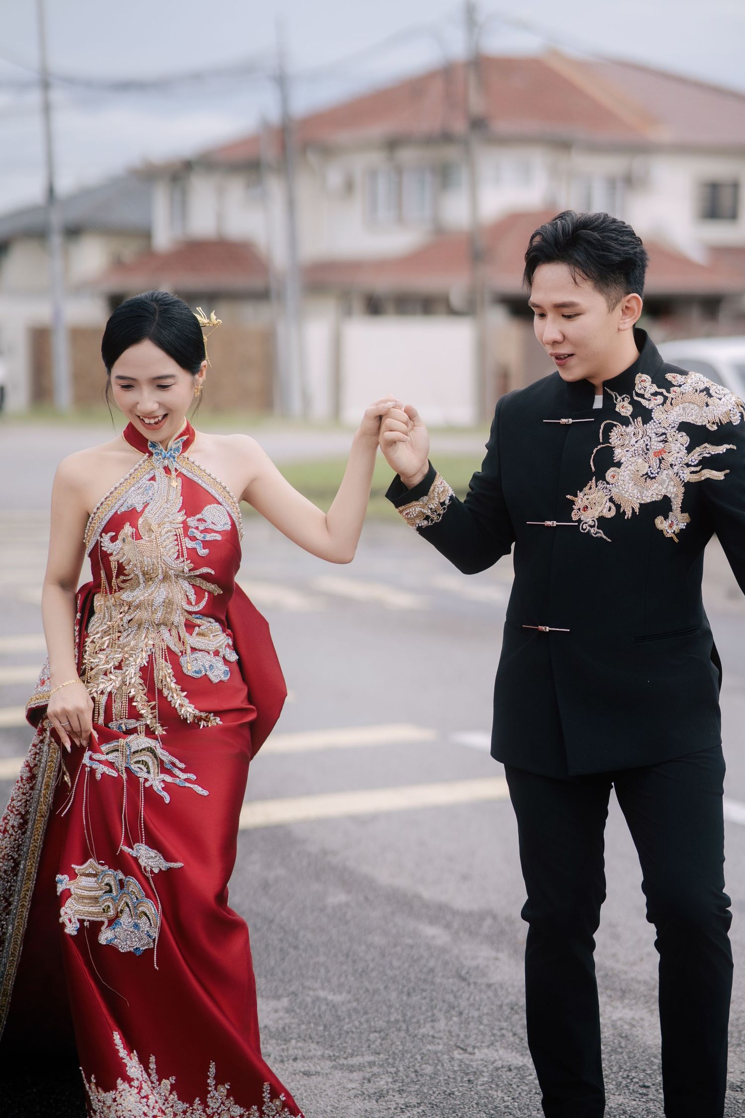 Bride smiles and lifts her dress while holding the groom's hand as they walk across a paved street