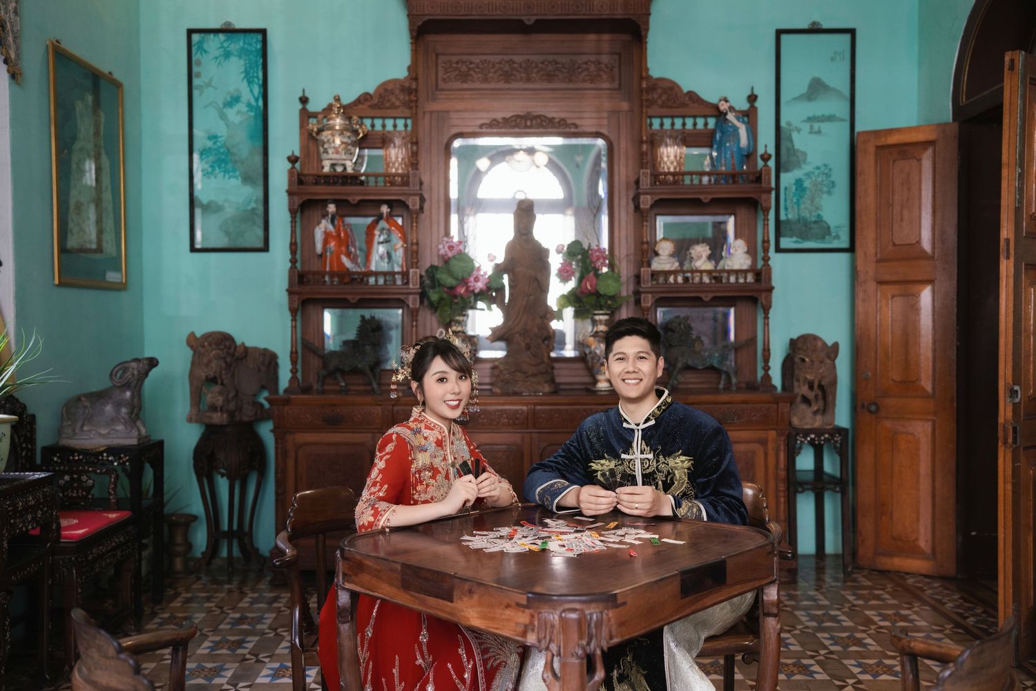 A couple enjoys a traditional game inside a heritage room at Pinang Peranakan Mansion, showcasing ornate wood-carved cabinets