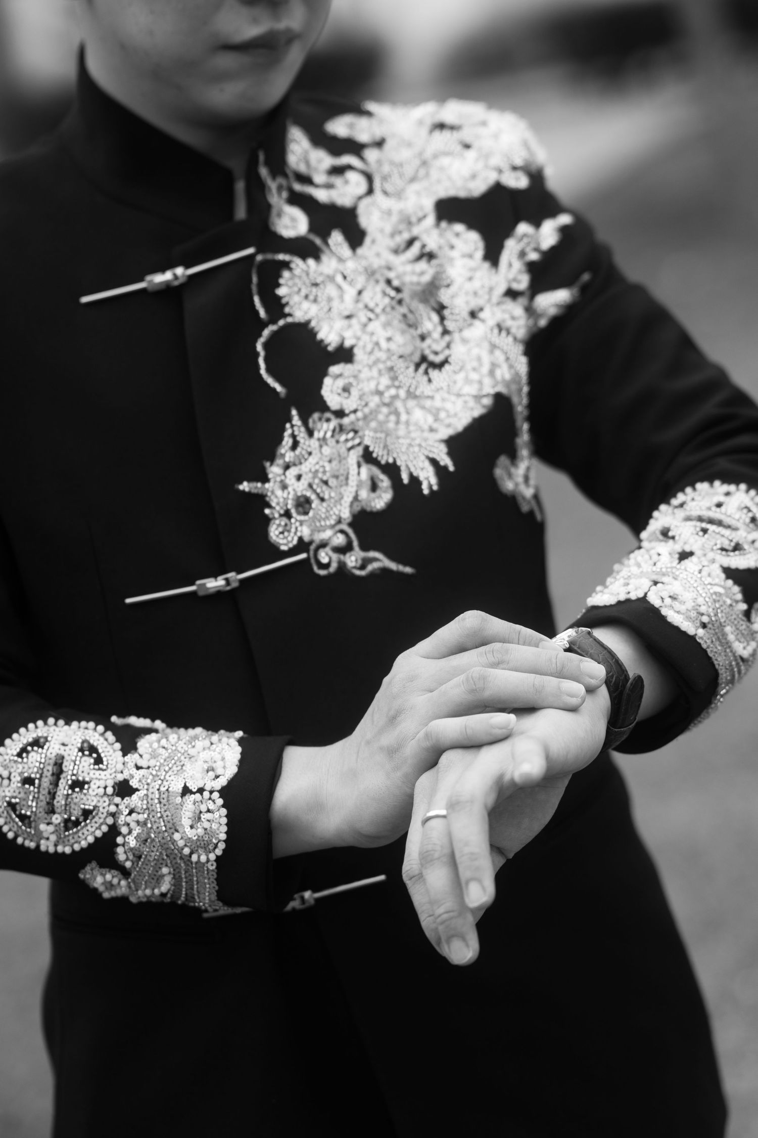 Black and white detail shot of traditional Chinese wedding jacket embroidery and the groom's wedding ring