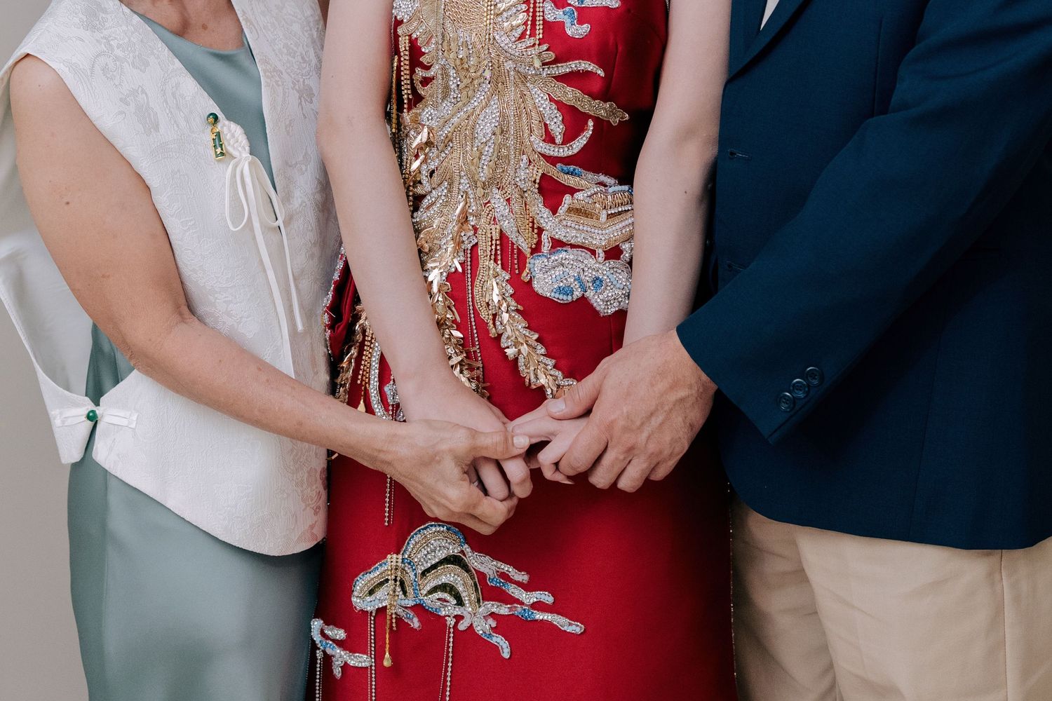 Parents holding the bride’s hands, featuring her red and gold embroidered traditional Chinese wedding dress